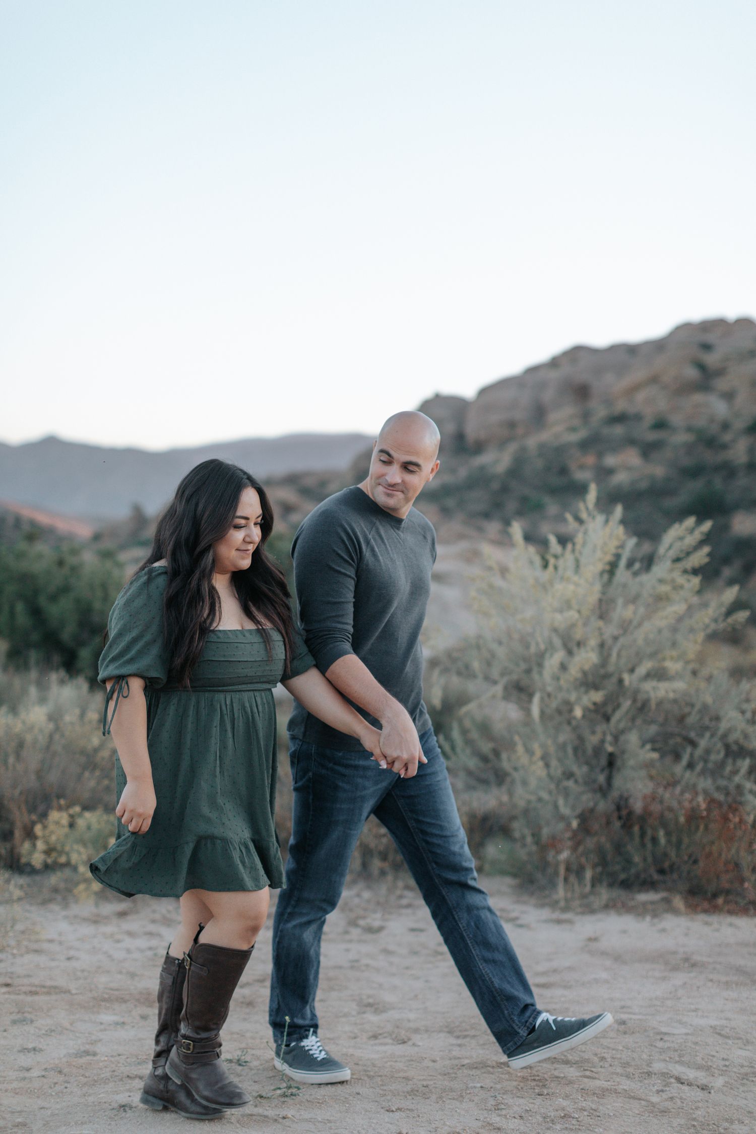 Playful couple dancing and laughing together in a desert landscape with brush and rocks.