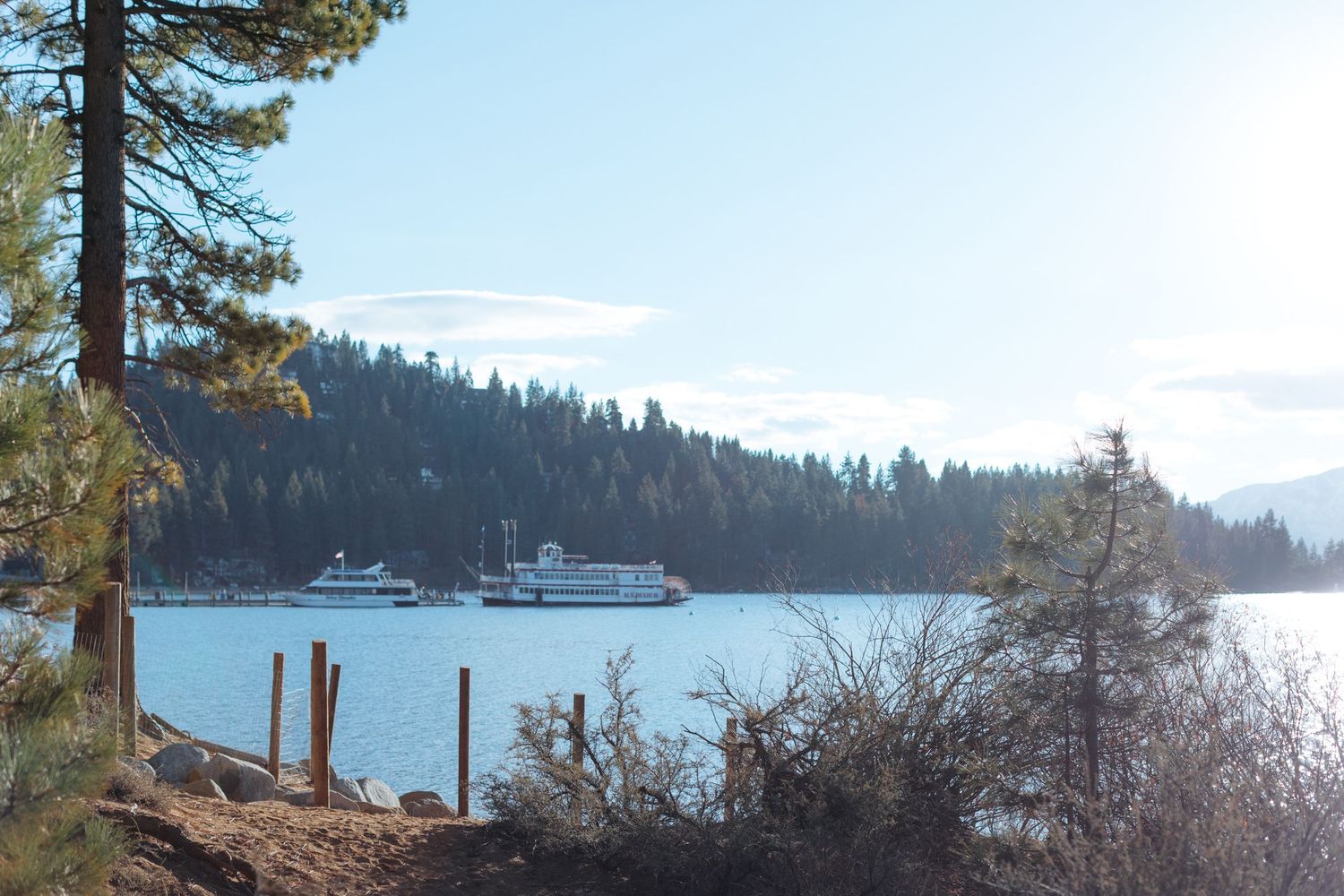Scenic mountain lake view with boats and evergreen trees along the shoreline.
