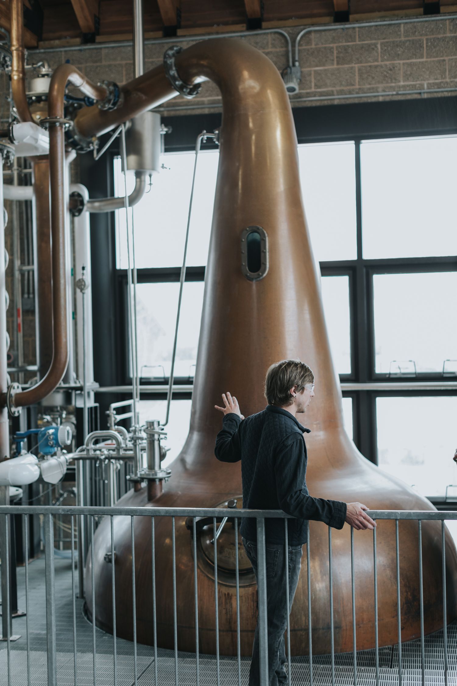 Large copper distillation equipment behind metal railings in an industrial facility.