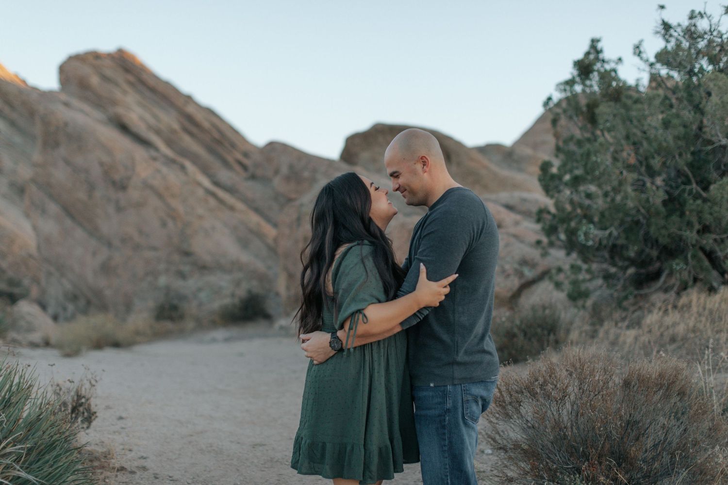 Two people share an intimate moment on a desert trail surrounded by rocky terrain.