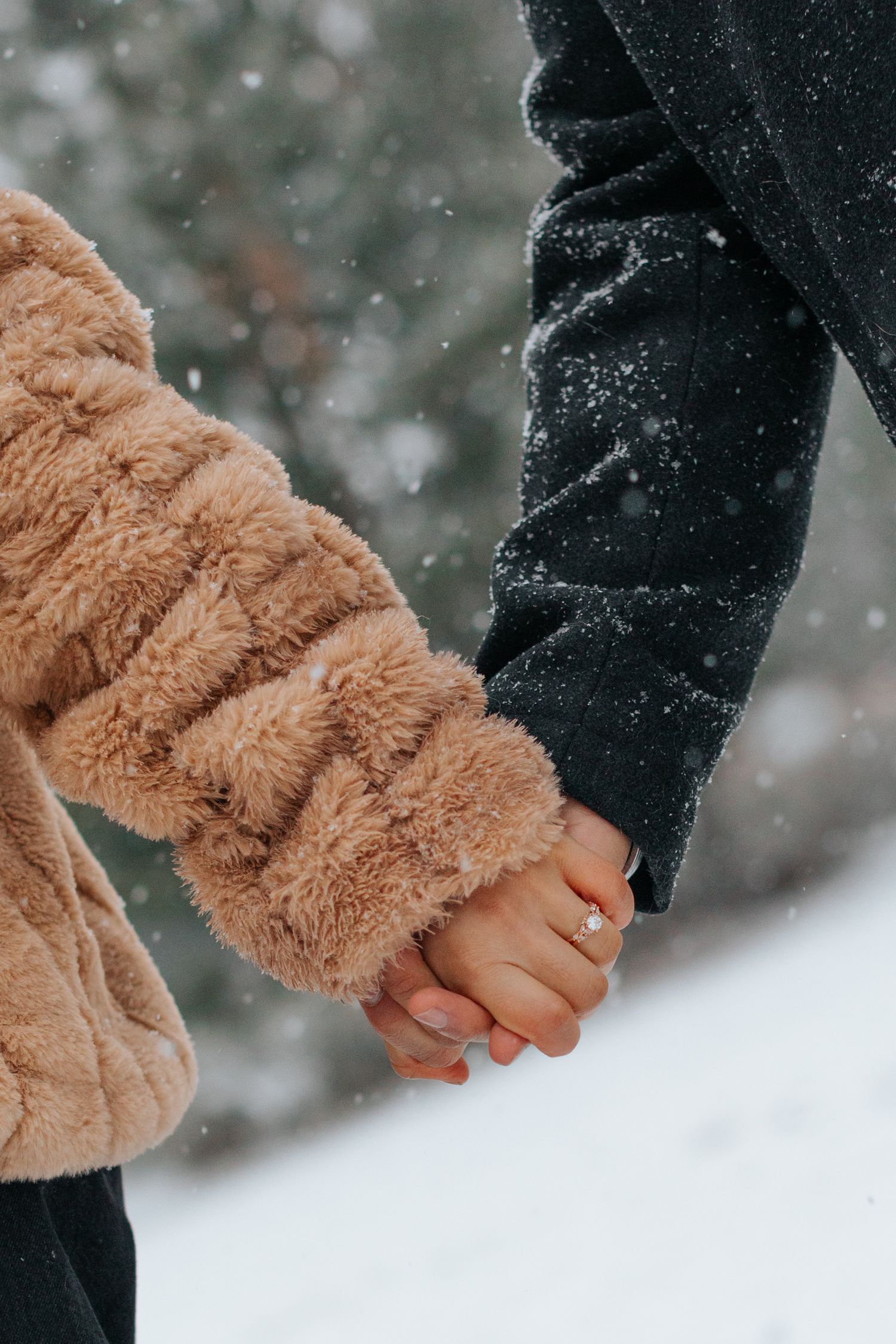 Close-up of couple holding hands in winter, showing engagement ring in the snow.