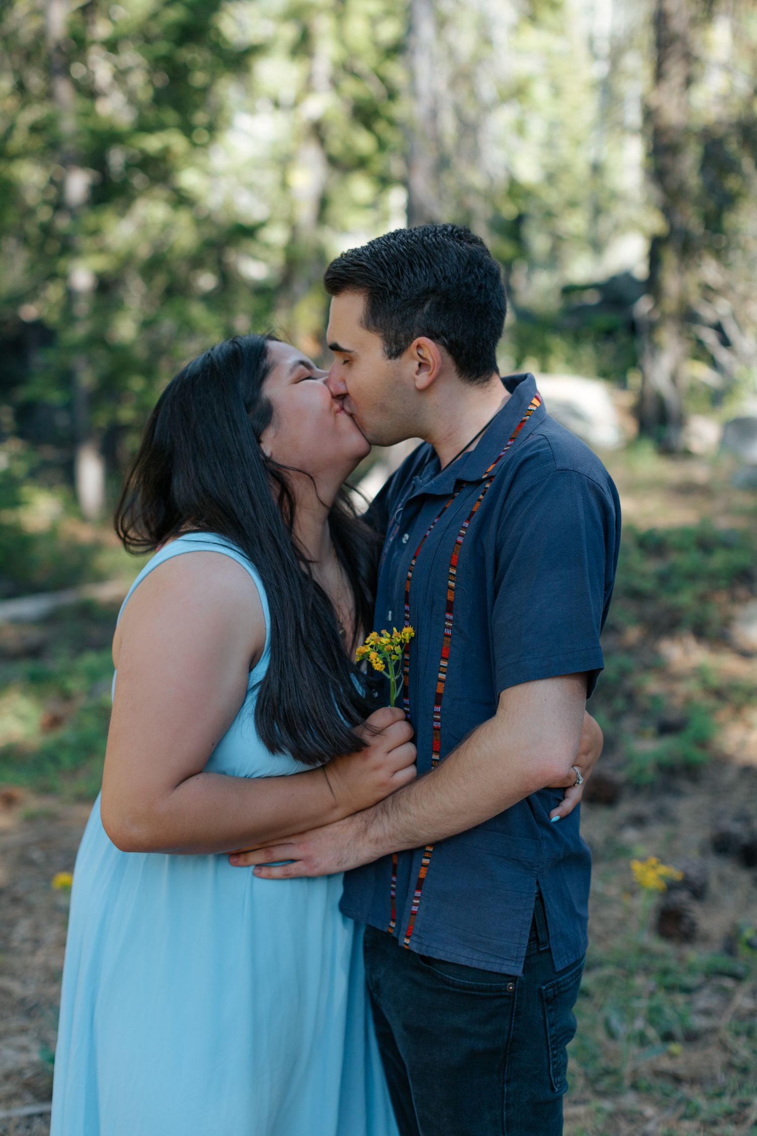 Romantic moment captured in a forest setting with sunlight filtering through trees.