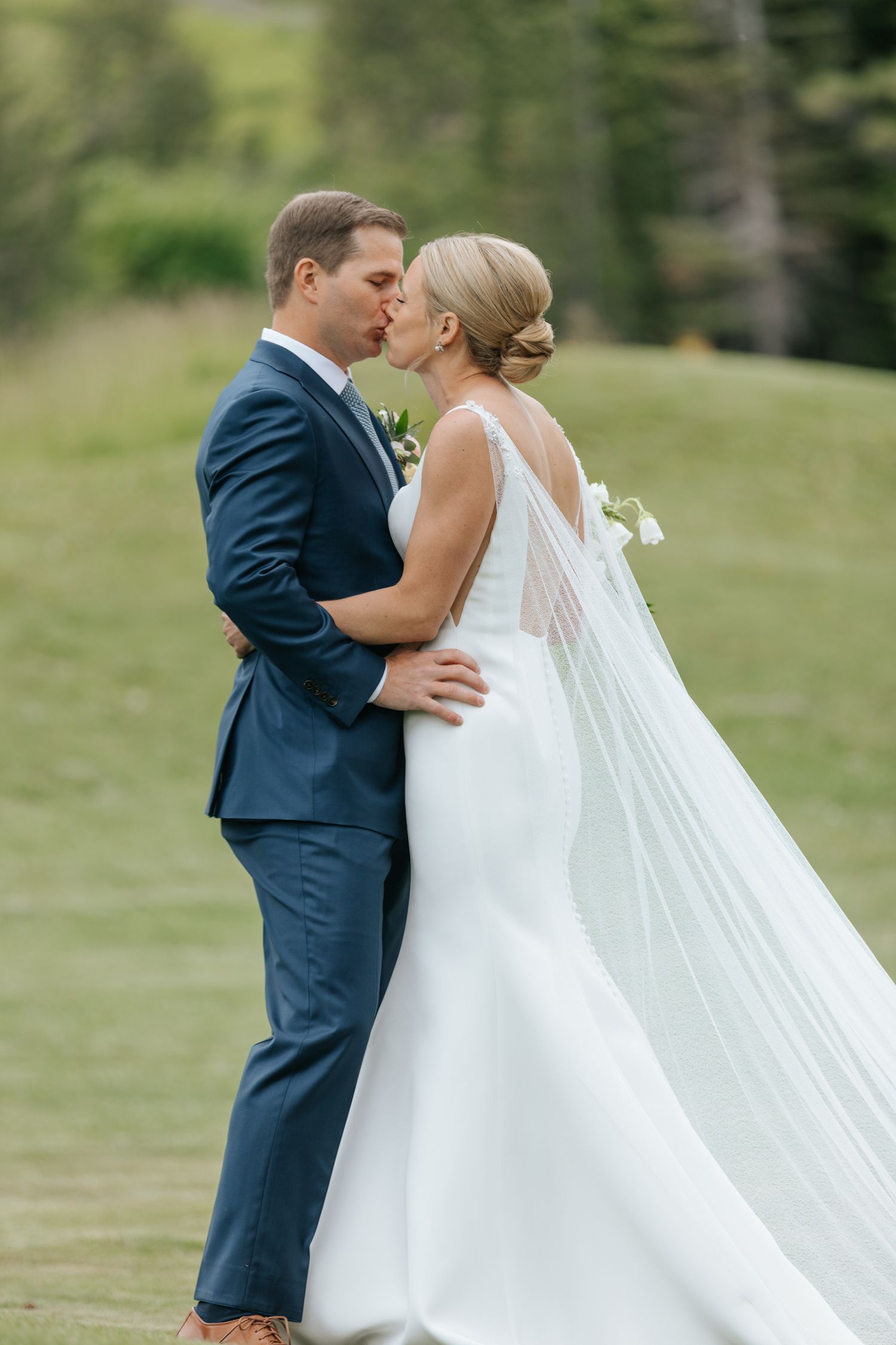 Romantic wedding couple shares an intimate kiss against a lush outdoor backdrop.