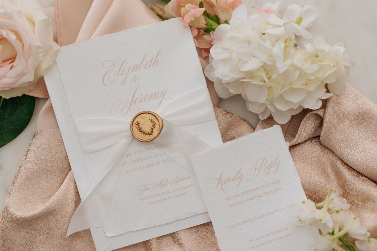 Wedding invitation suite with white and pink paper, wax seal, and delicate floral details.