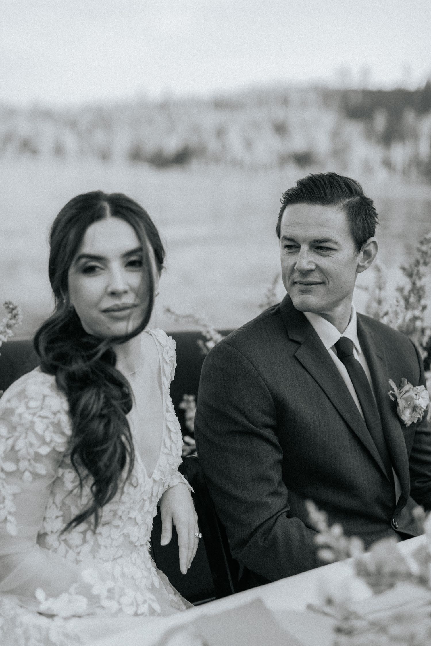 A black and white wedding portrait of a couple in formal attire with the bride wearing a lace dress.