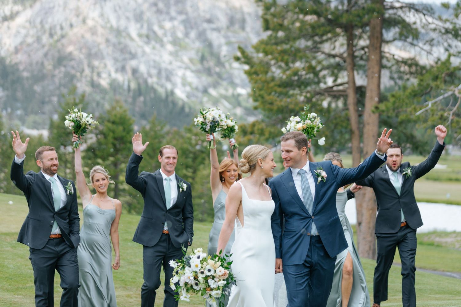 Wedding party celebrates with arms raised in joy against mountain landscape.