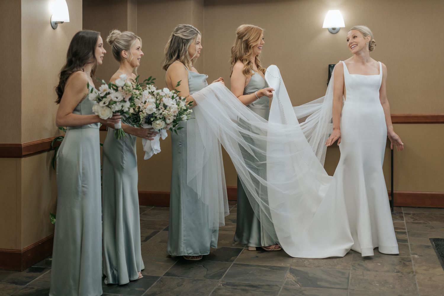 Bridesmaids in sage green dresses helping with wedding preparations indoors.