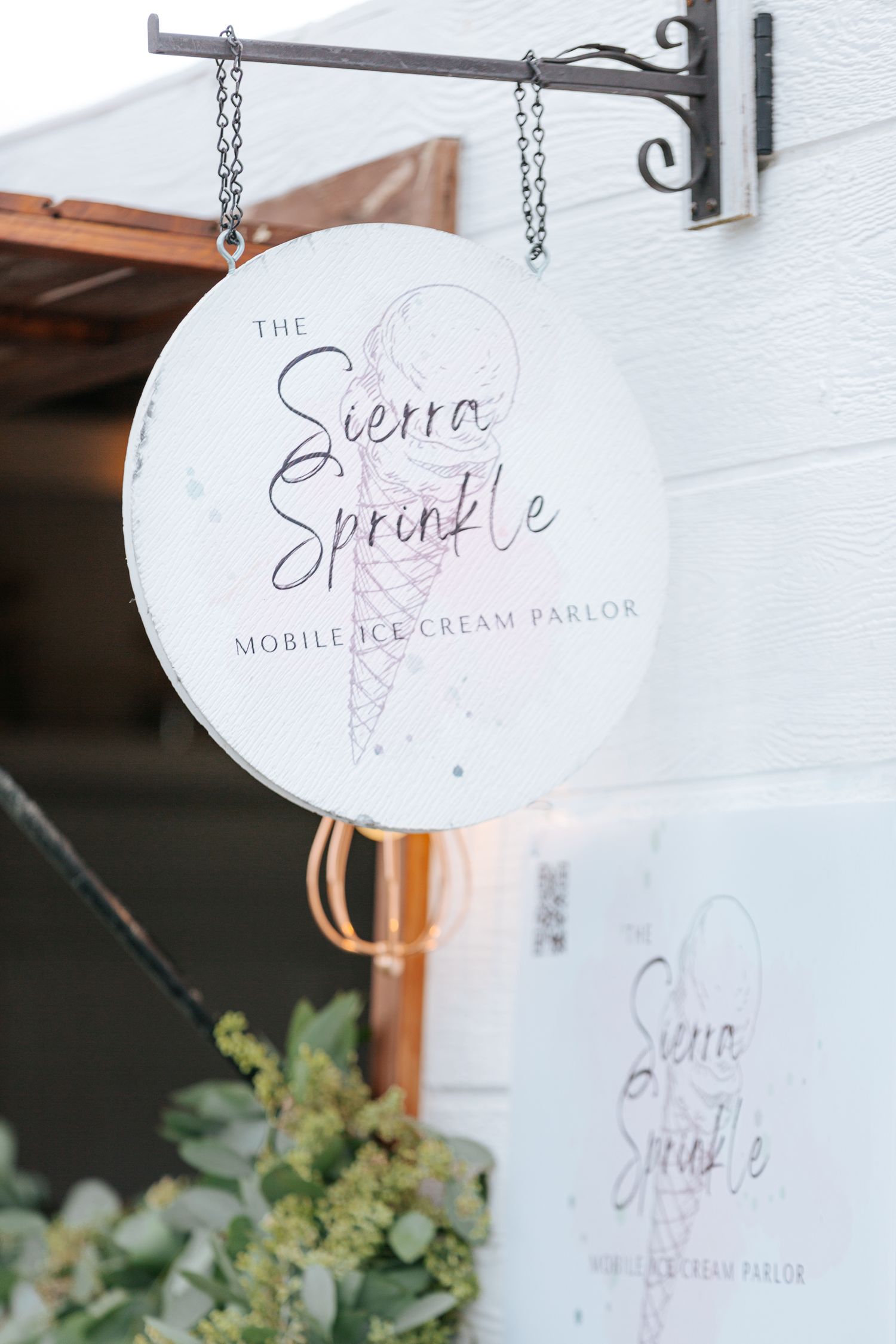 White hanging sign for mobile ice cream parlor with elegant script lettering.