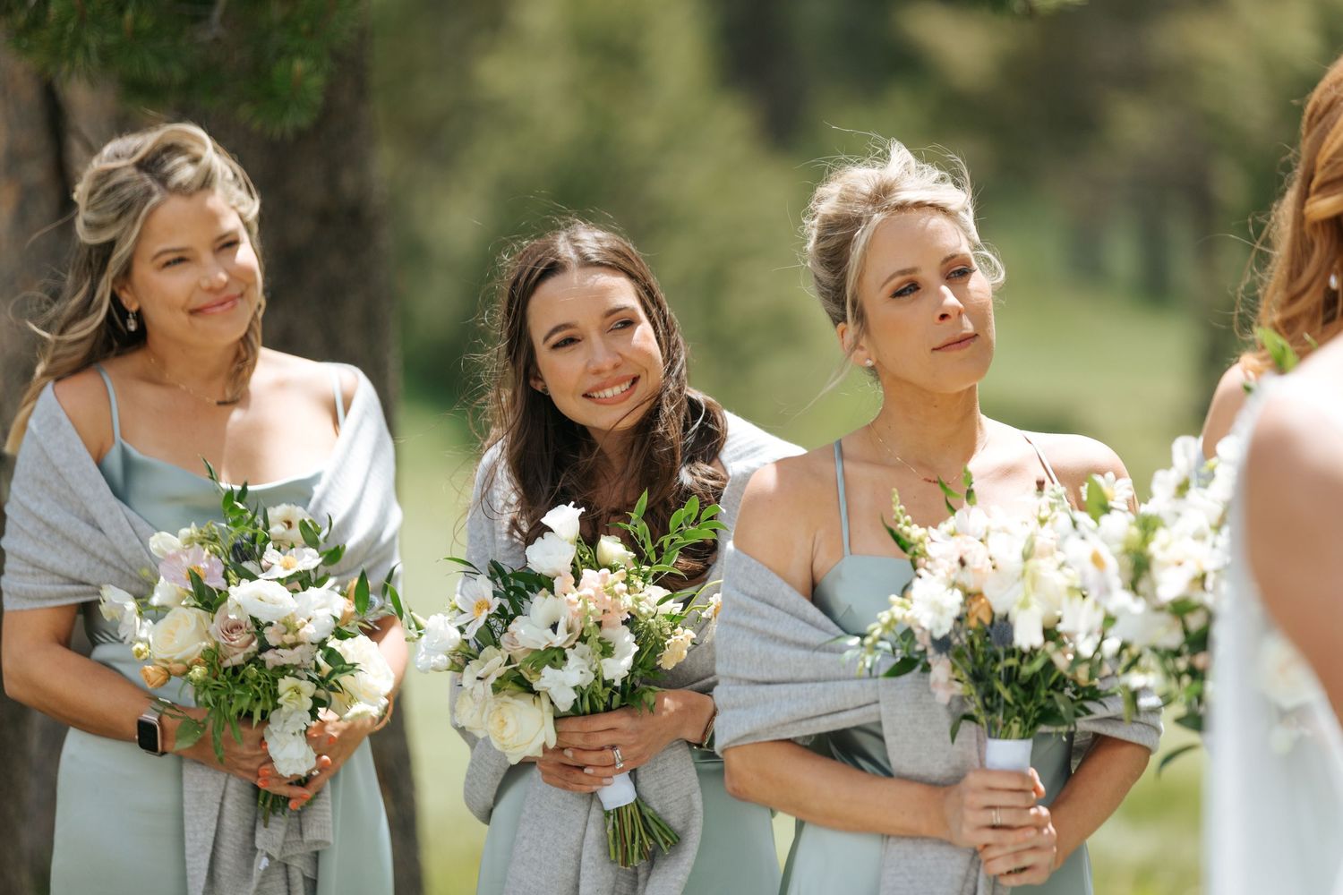 Bridesmaids in light colored dresses hold white and green floral bouquets.