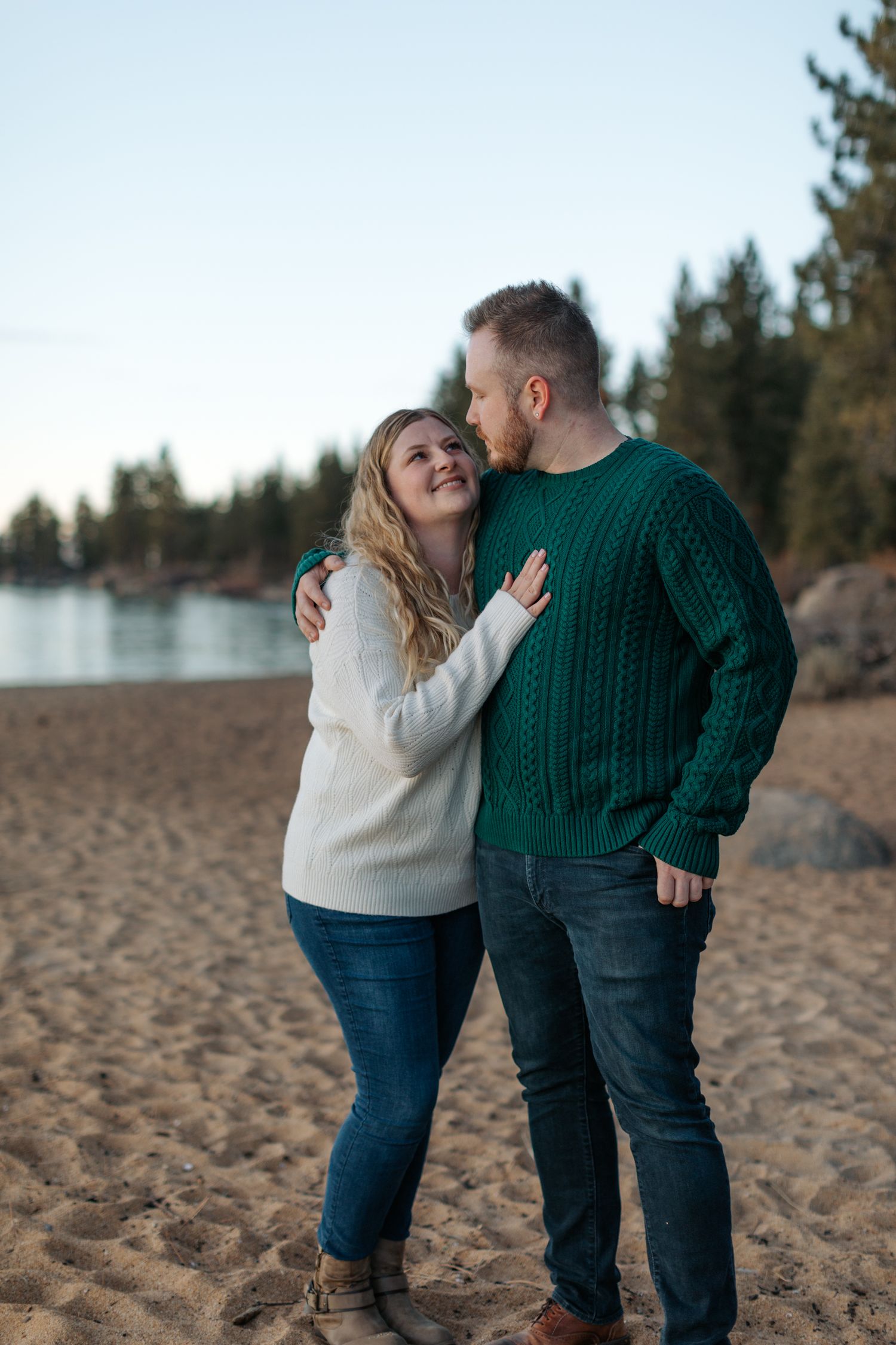 Couple in matching sweaters sharing romantic moments on a sandy beach.