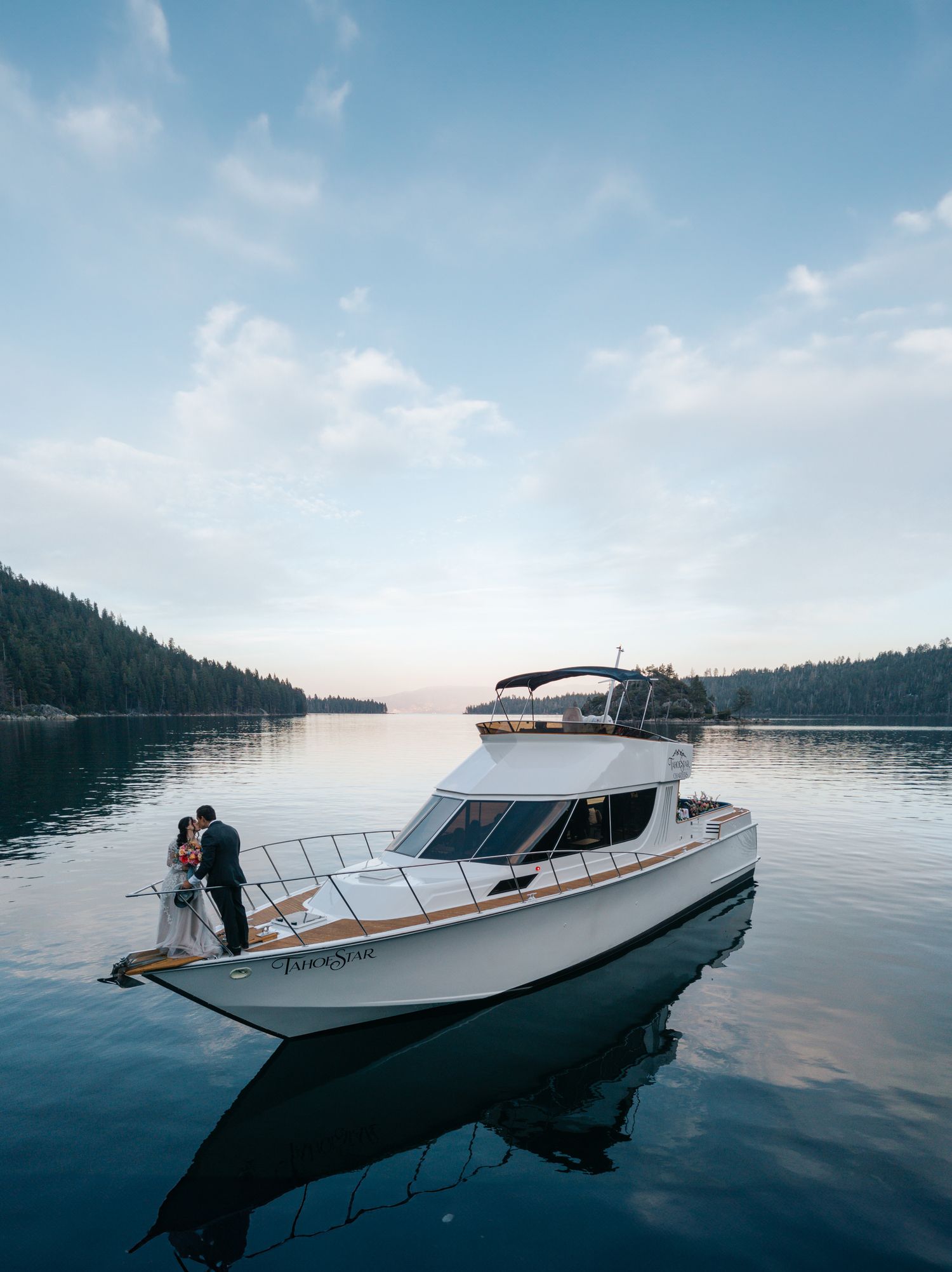 A sleek white yacht cruises on calm waters at dusk with forested mountains in the background.