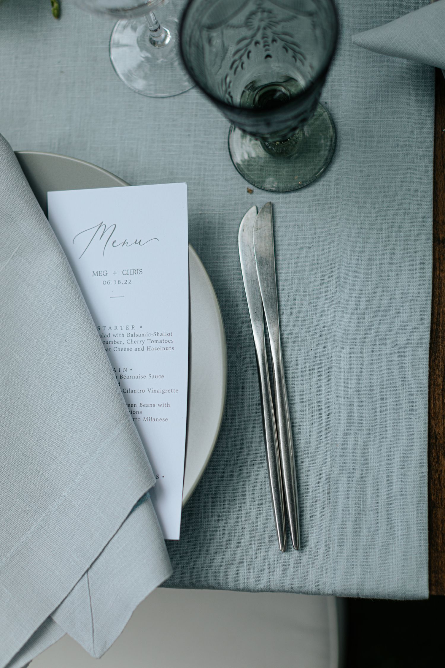 Wedding menu and place settings arranged on a light gray linen tablecloth.
