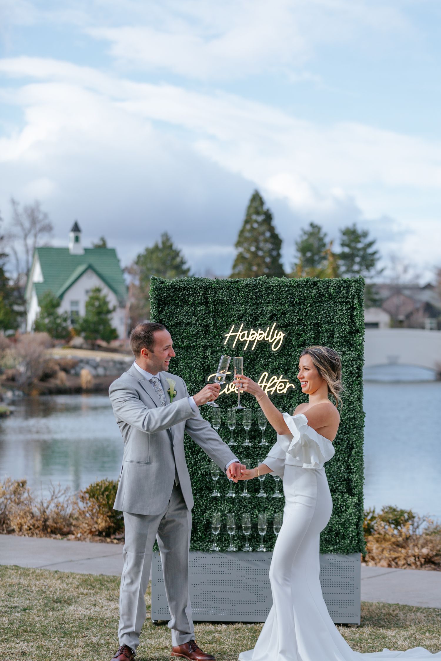 Wedding couple dancing and celebrating by lakeside with green hedge wall backdrop.