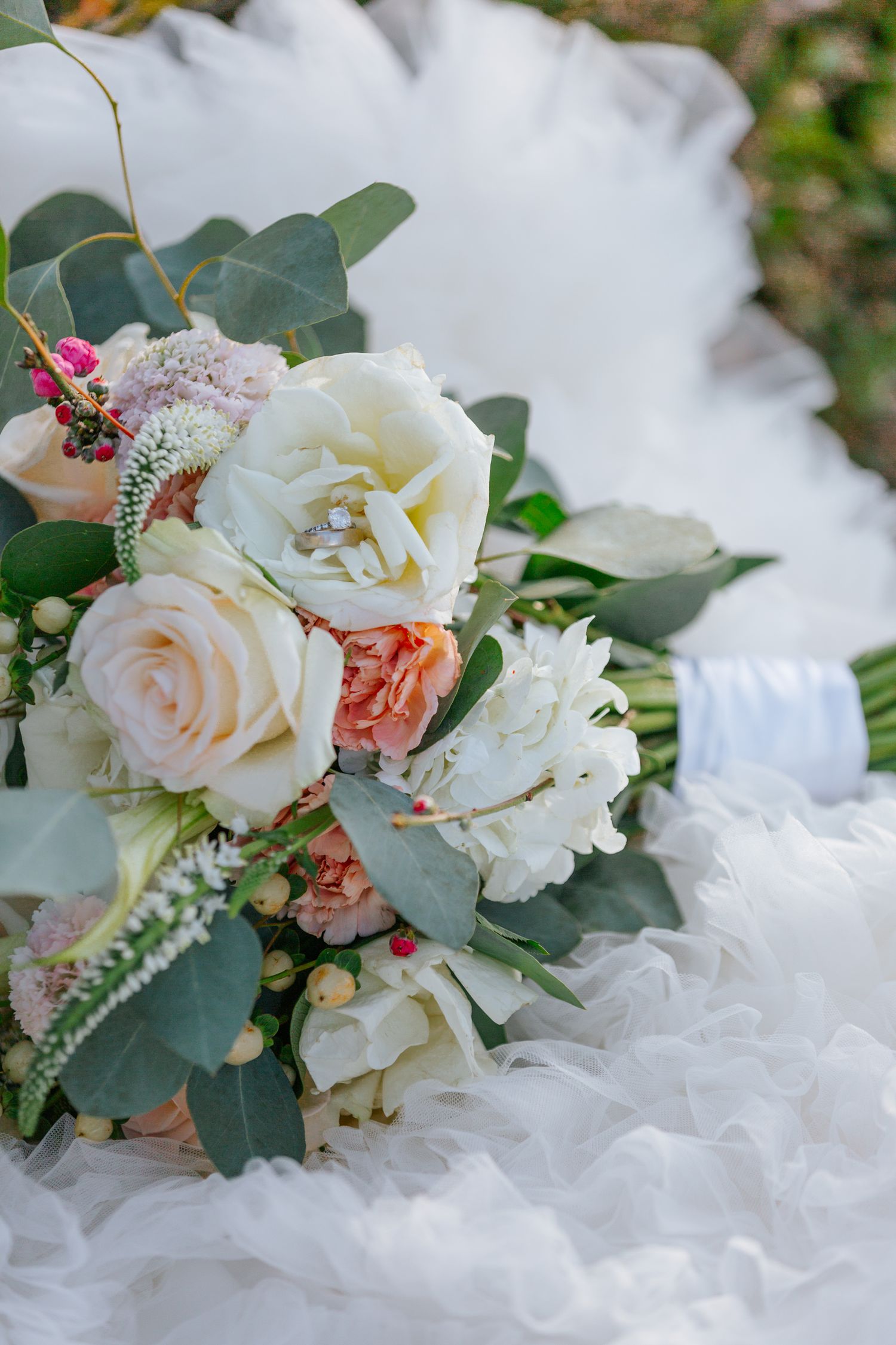 A romantic wedding bouquet with white roses, pink flowers, and eucalyptus leaves.