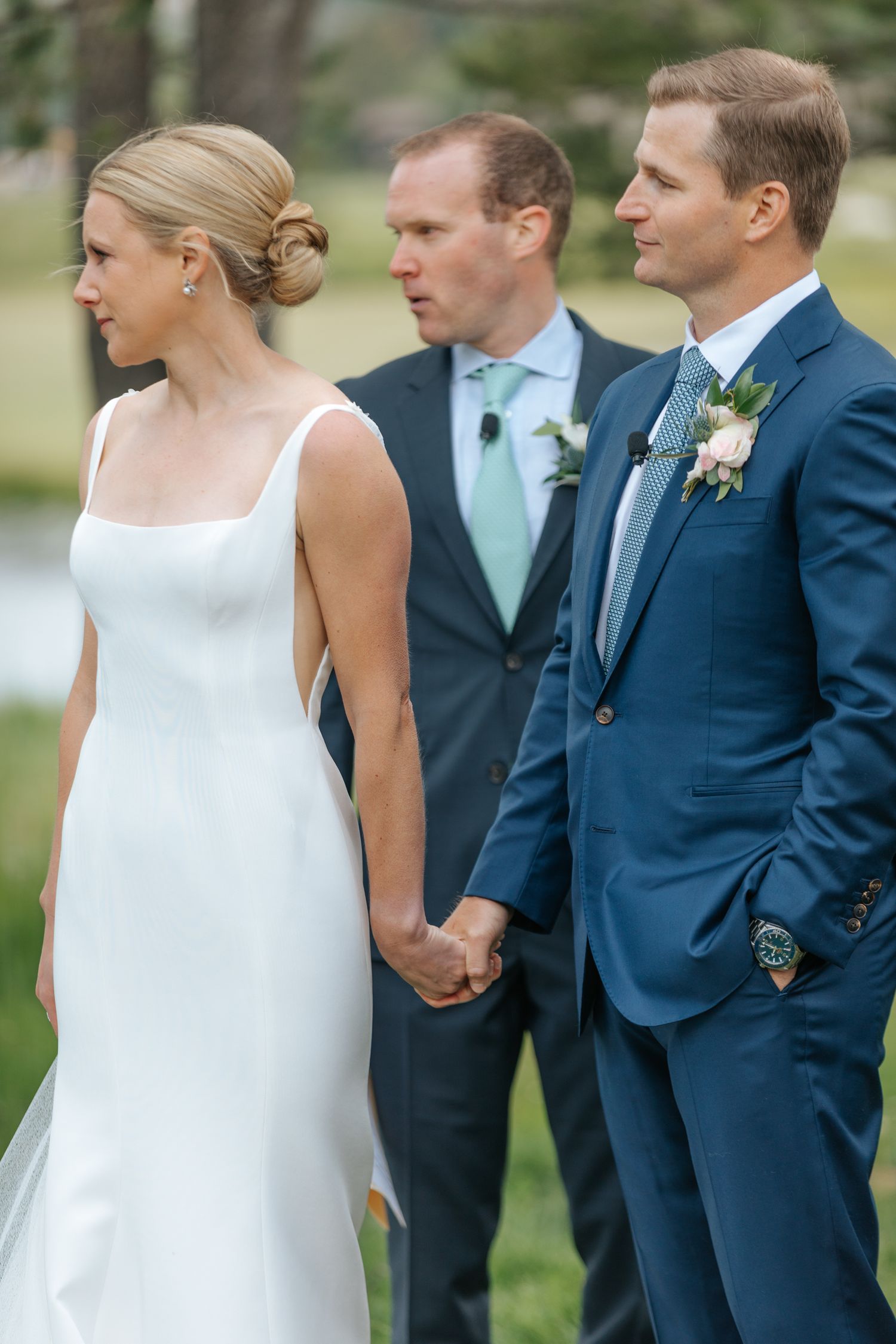 Wedding party in navy suits and white dress lined up during outdoor ceremony.