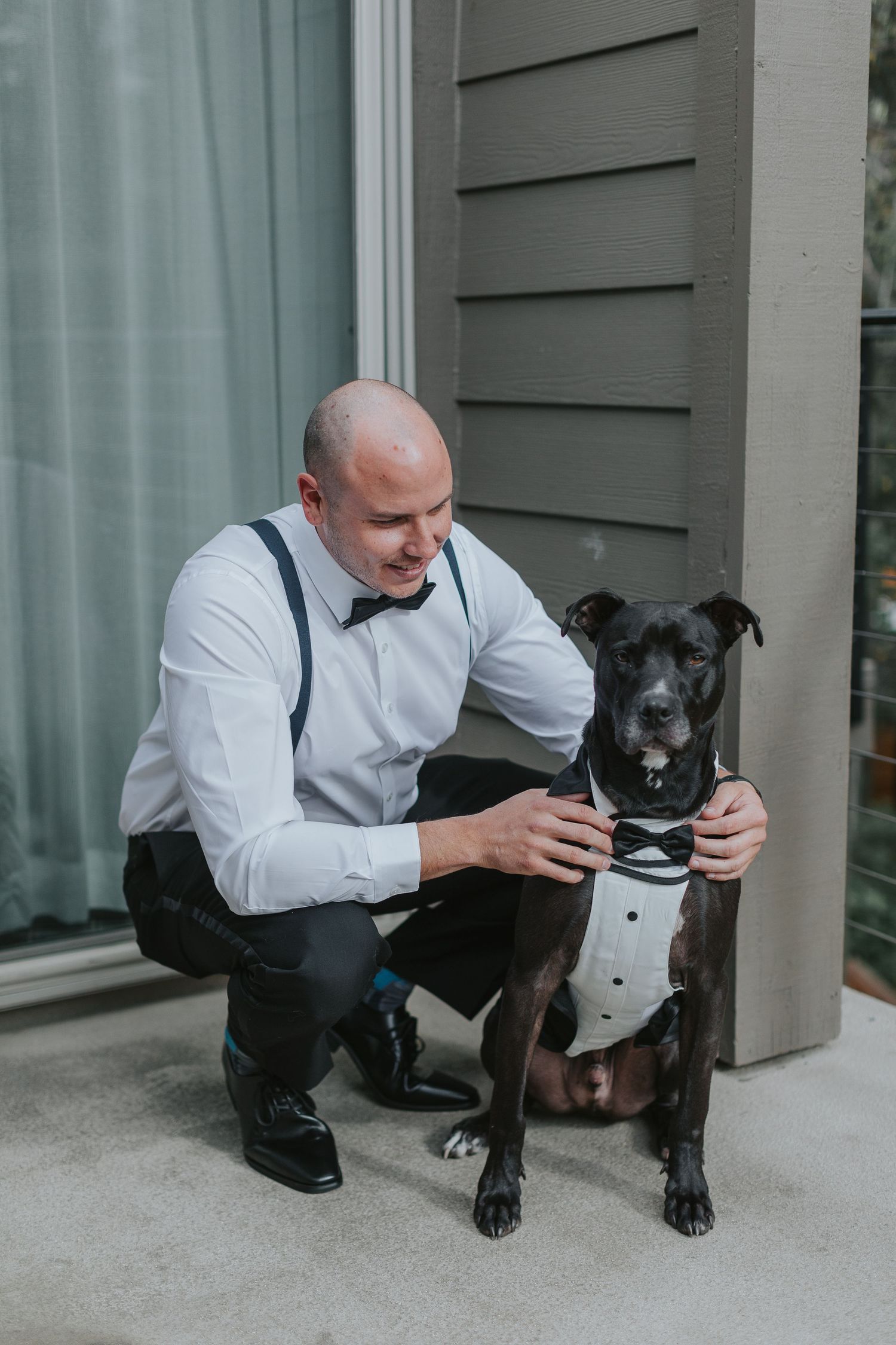 Person in formal attire kneeling next to black dog on porch.