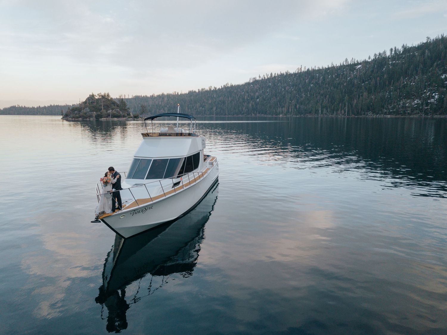 White yacht floating on calm waters with mountain landscape in background during sunset.