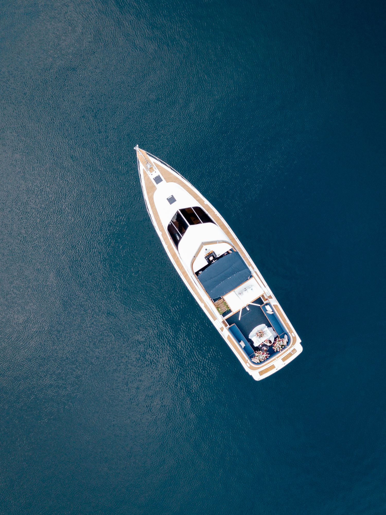 Aerial view of a white yacht floating on deep blue waters near a forested shoreline.