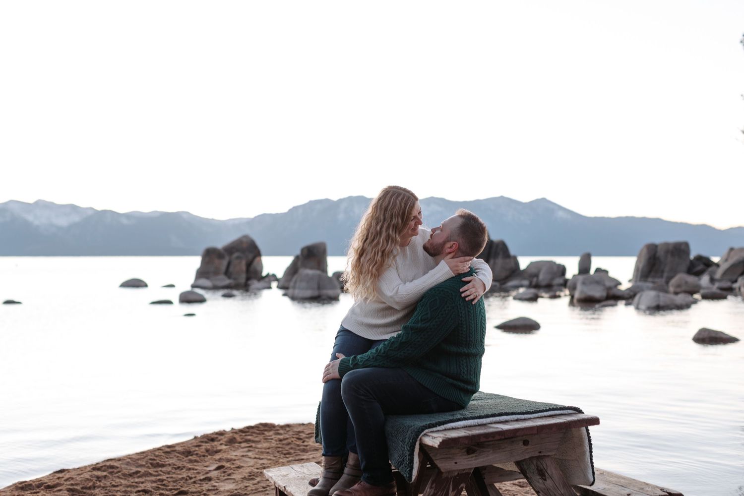 Romantic beach photoshoot with mountain views and calm waters in the background.