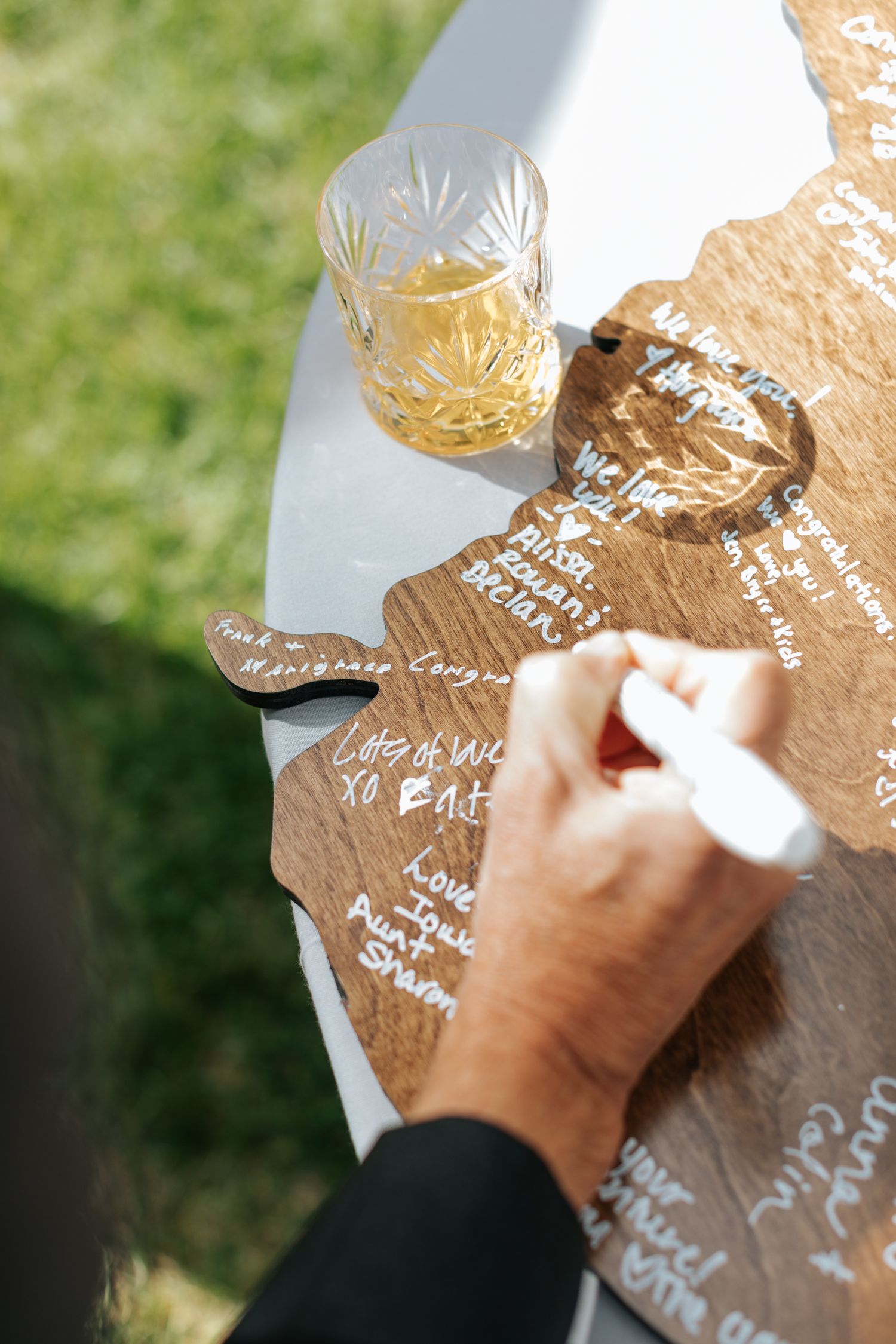 Close-up of hands writing on a wooden puzzle piece at an outdoor event.