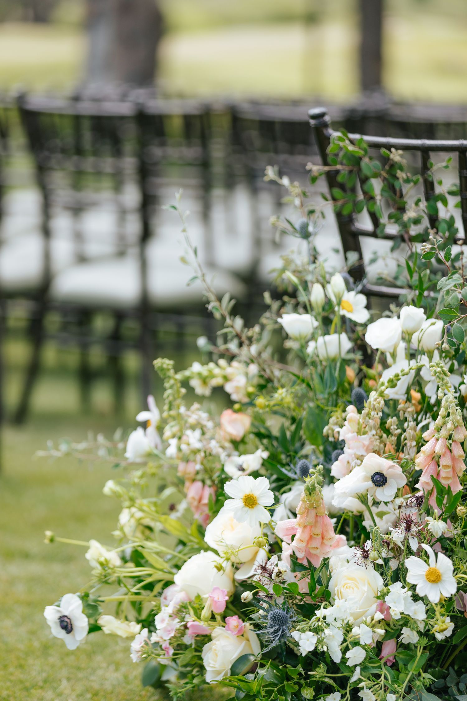 Delicate white and pink floral arrangements line the outdoor wedding ceremony space.
