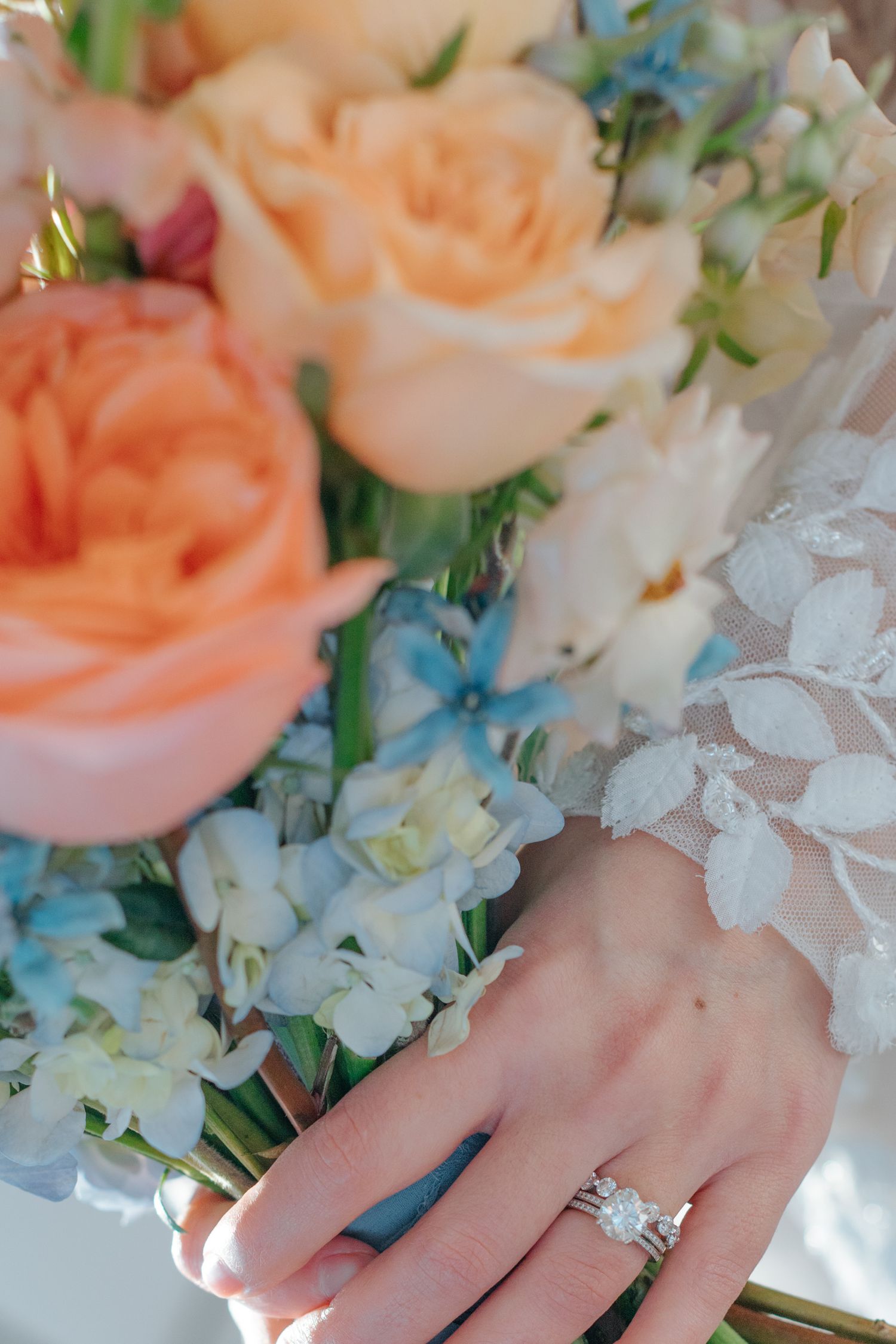 Close-up of engagement ring among peach roses and white floral arrangements.