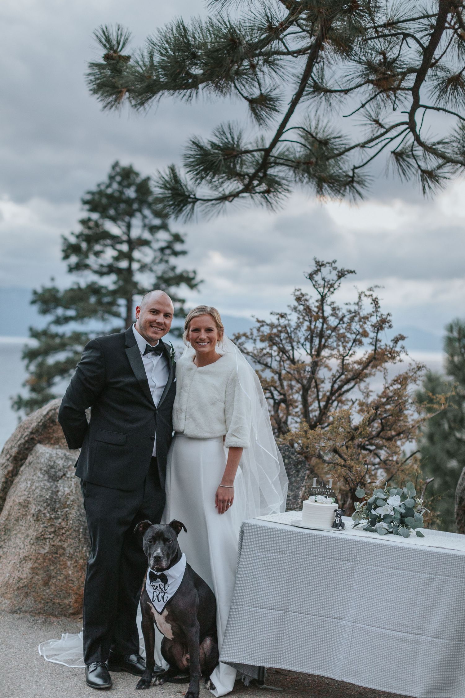 Wedding couple posing with their black dog on a white tablecloth outdoors.