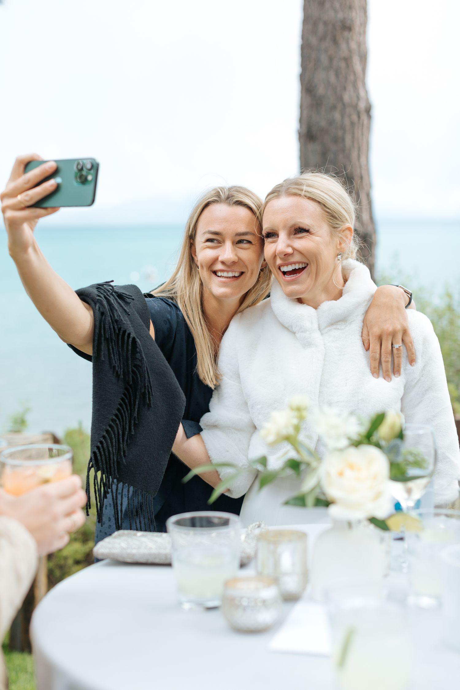 Wedding guests taking selfies and laughing at an outdoor reception table.