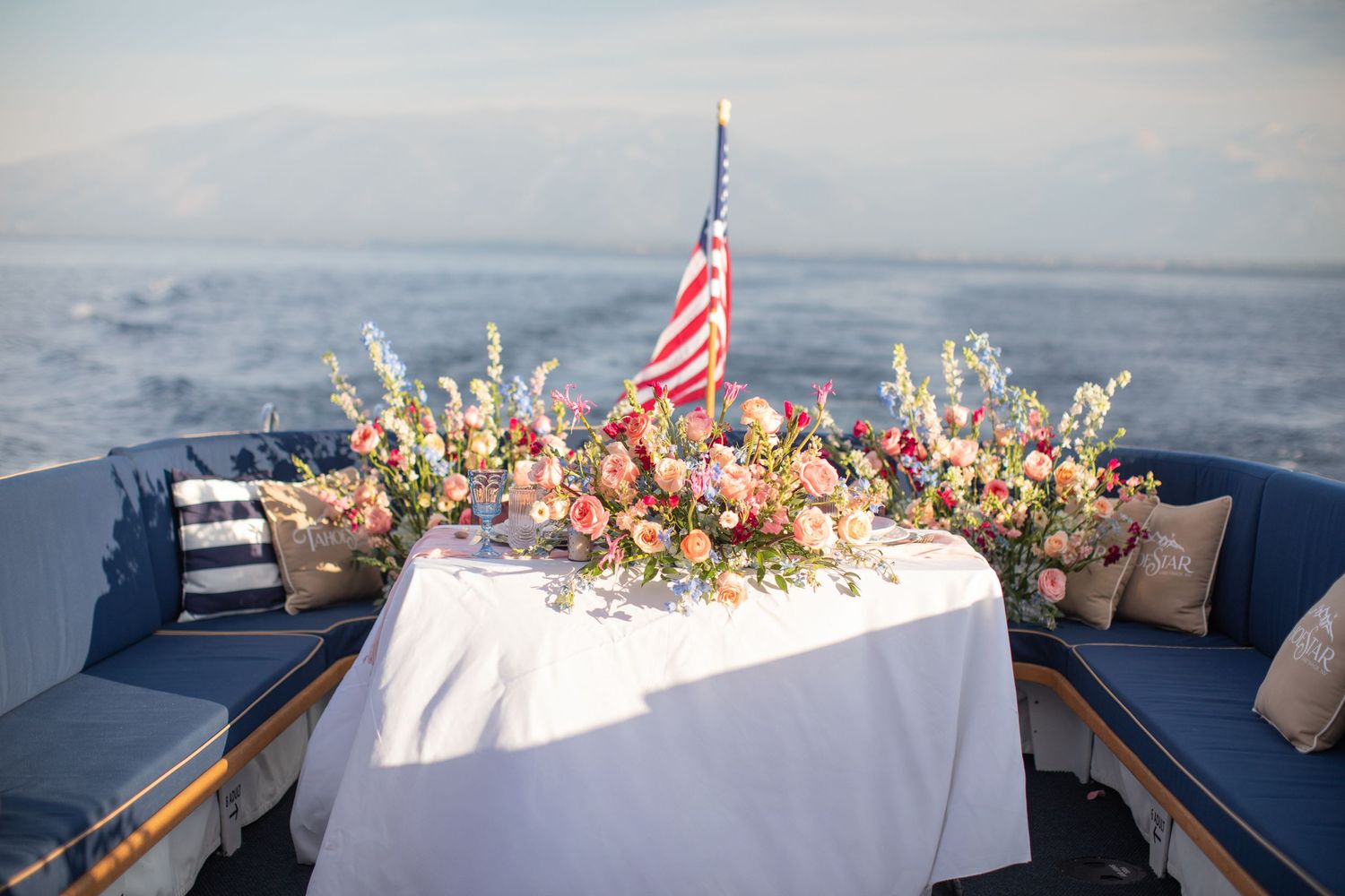 Elegant boat deck table setting with floral centerpiece and American flag against ocean view.