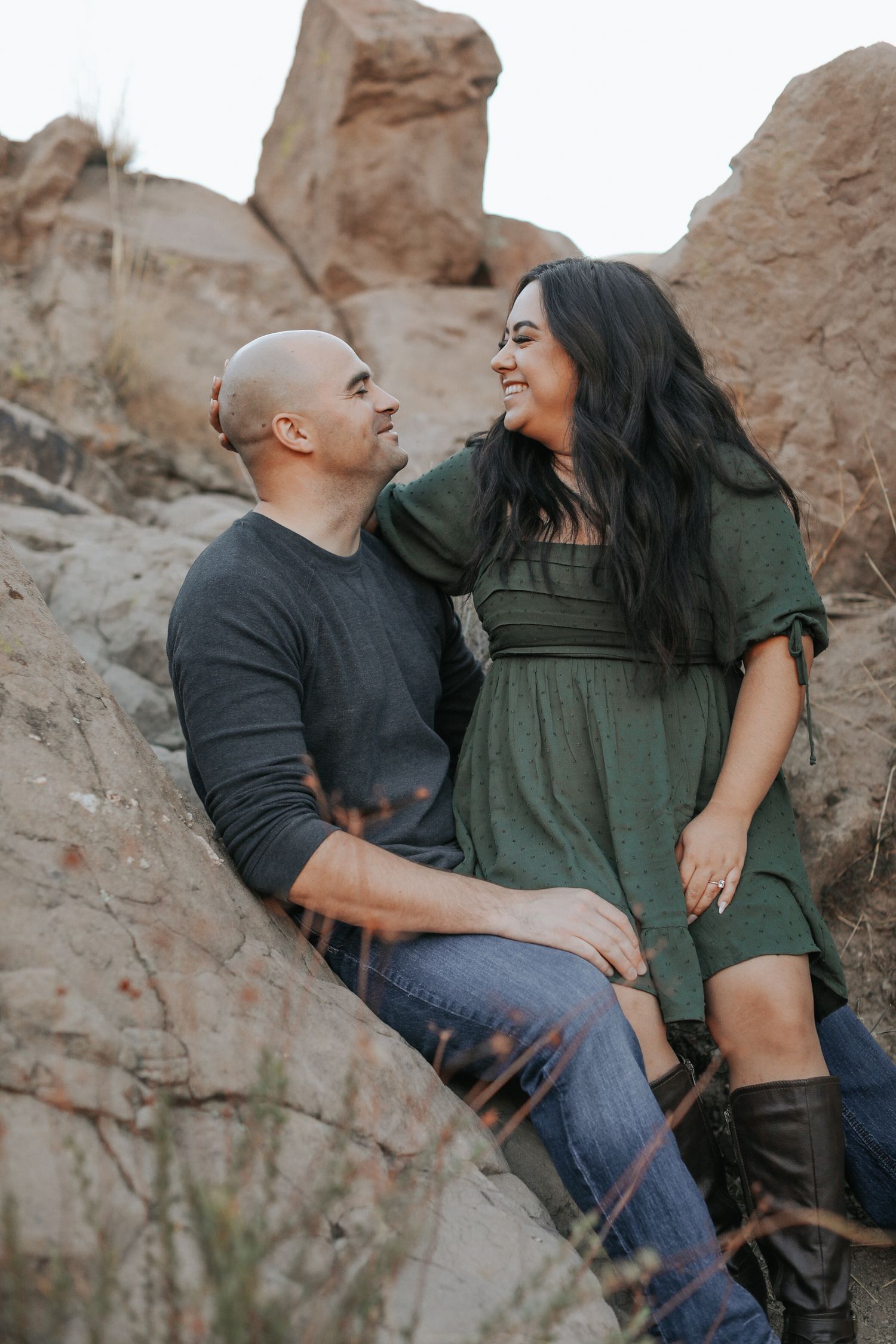 A couple sits playfully on desert rocks during a sunset photoshoot.