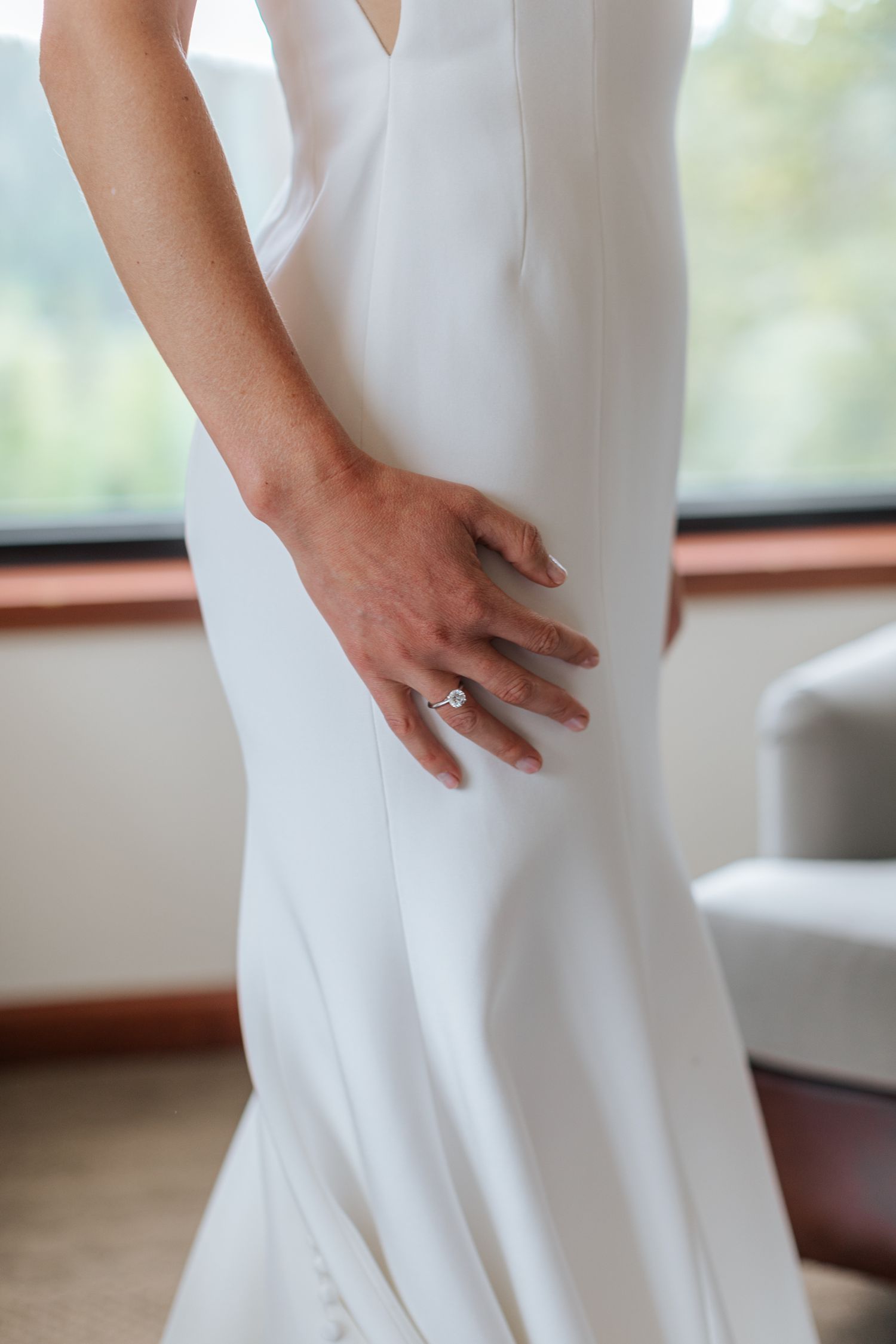 Close-up of a white wedding dress and engagement ring on the bride's hand.