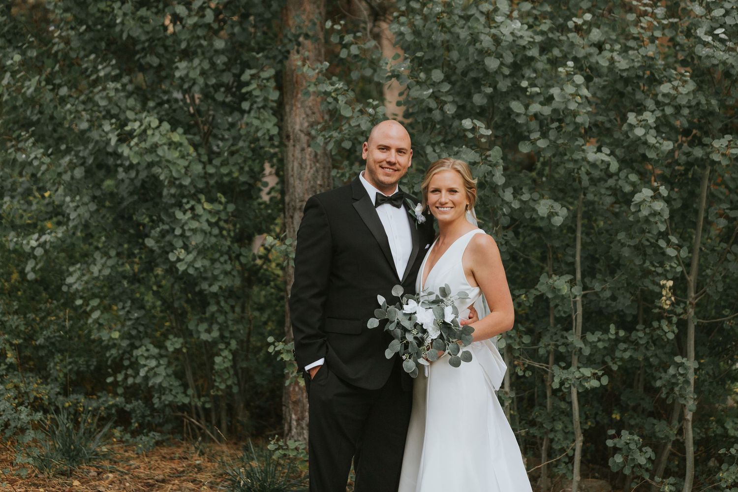 Wedding couple shares romantic moments among pine trees in an outdoor setting.