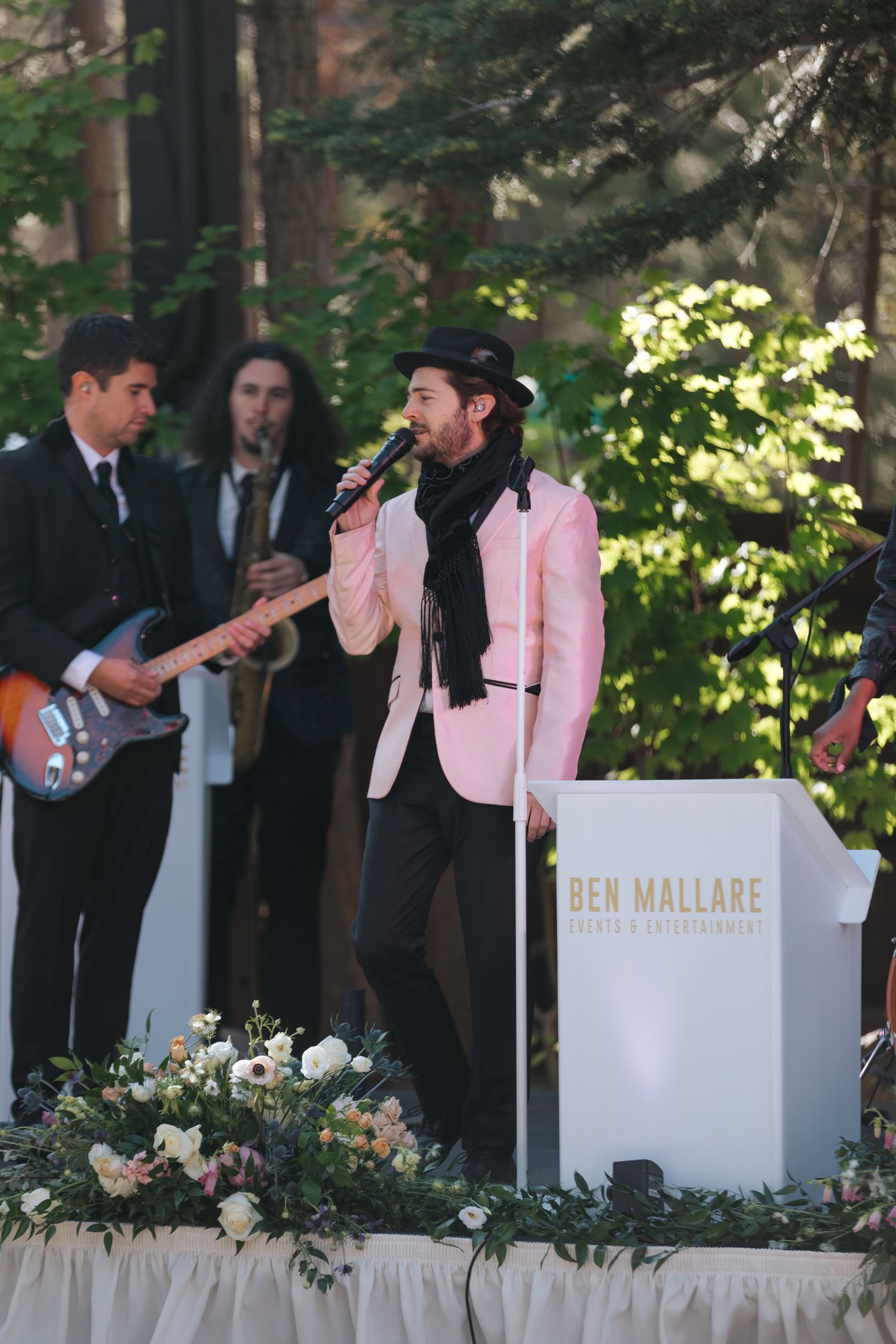 Live band performing at outdoor wedding with white decorative panels and floral arrangements.