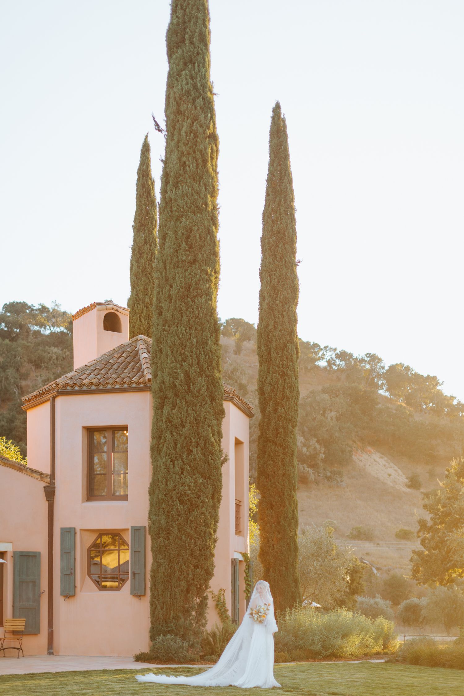 Elegant pink Spanish-style building with arched doorways and cypress trees at sunset.