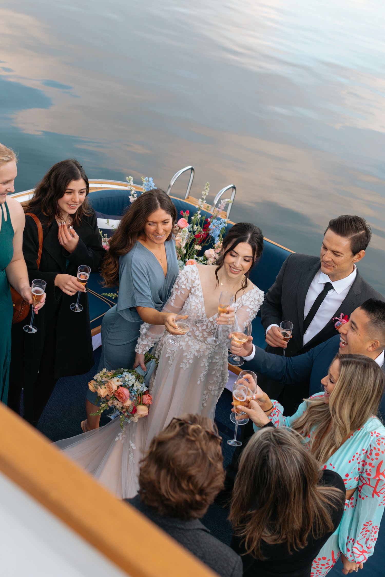Wedding party socializing and toasting on boat deck with lake views.