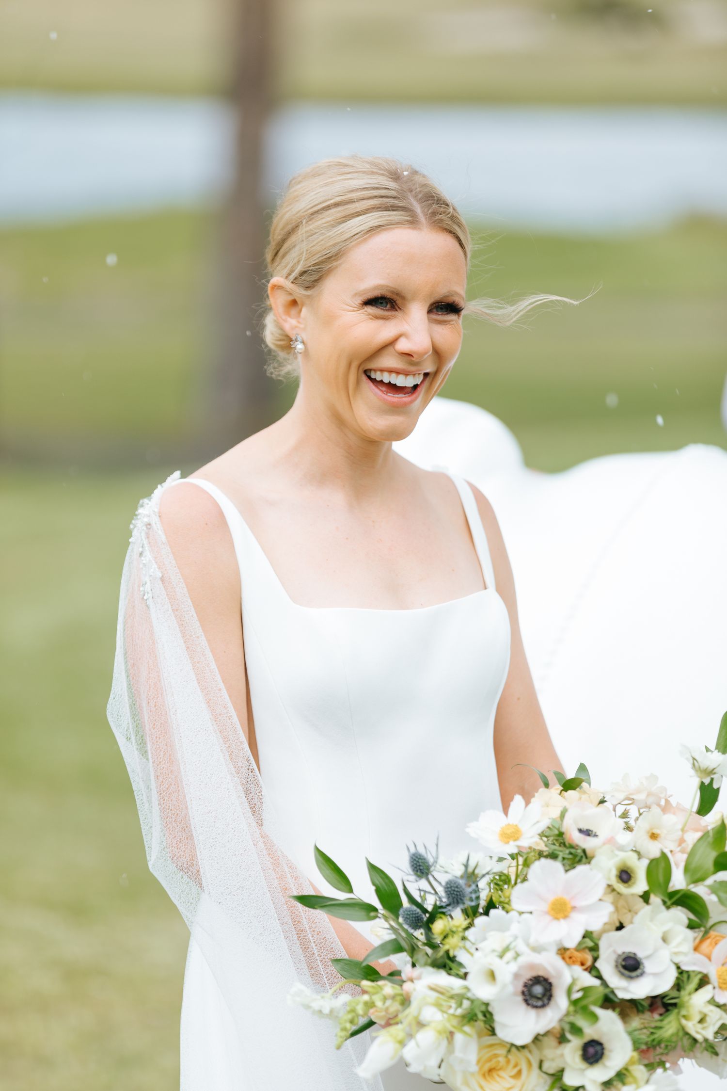 Bride holding a beautiful white and green floral bouquet smiles joyfully outdoors.
