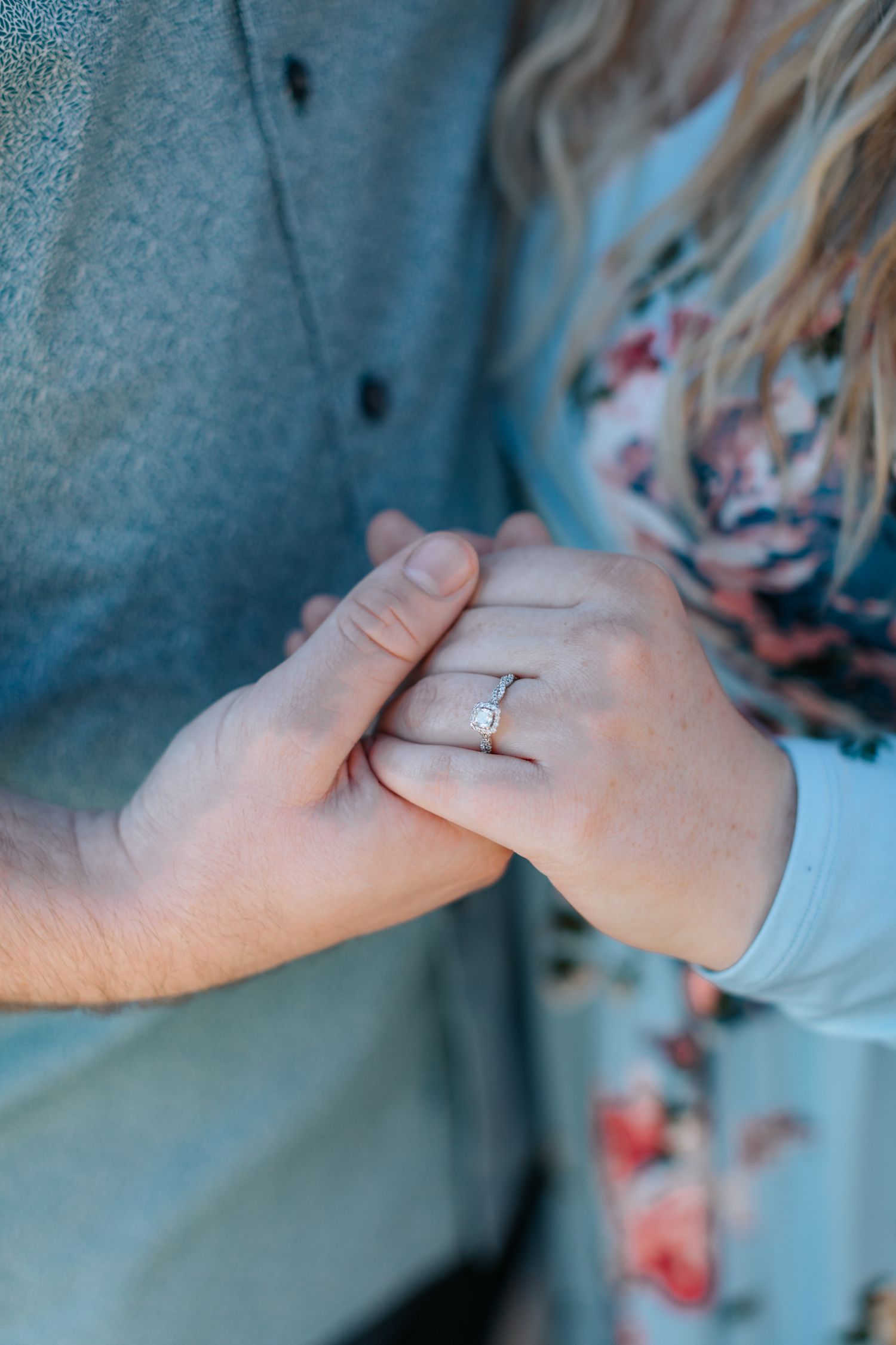 Close-up of hands showing engagement ring against blue background.
