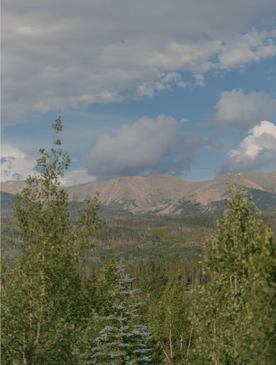 Panoramic mountain landscape with aspen trees and scattered clouds over rugged peaks in Colorado.