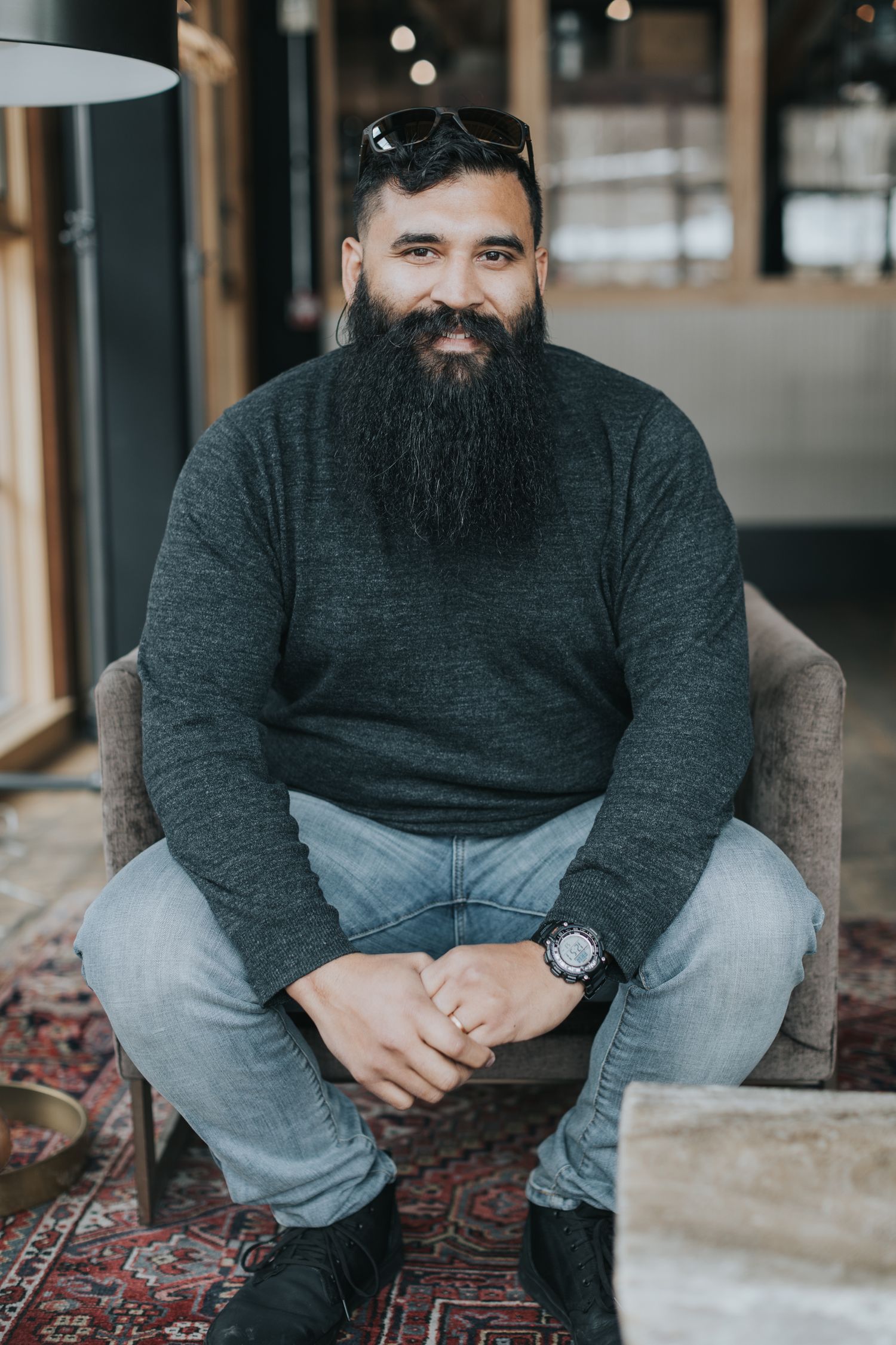 Person seated on patterned carpet in casual attire against industrial backdrop.