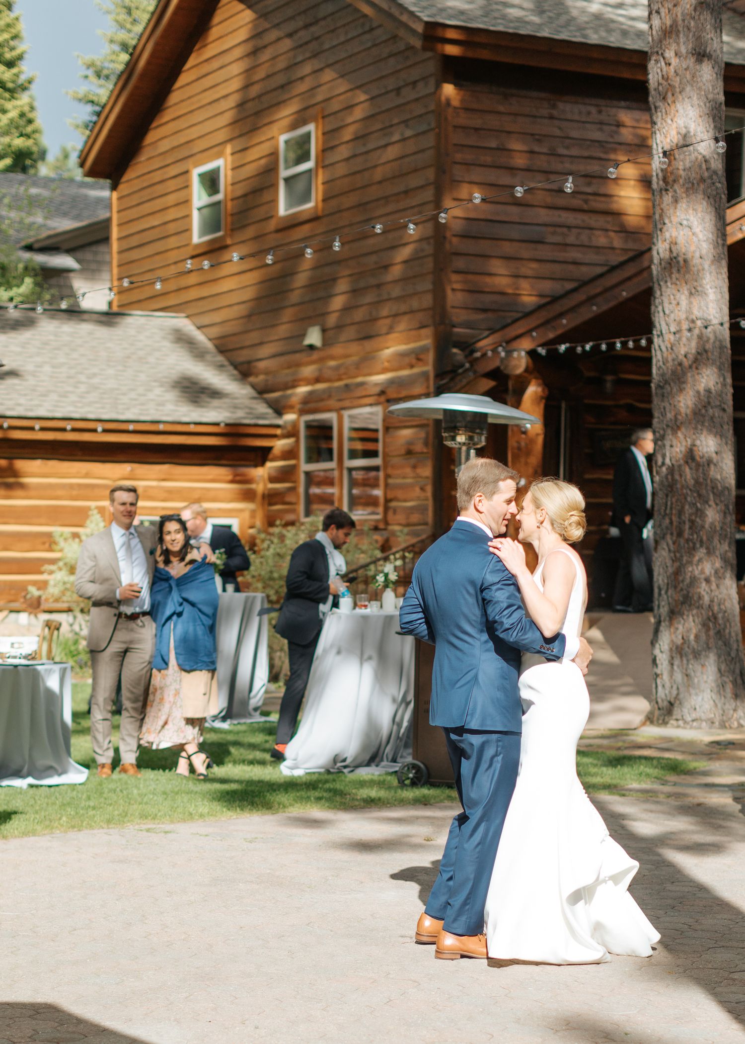 Couple dancing together outside a rustic wooden cabin during a wedding celebration.