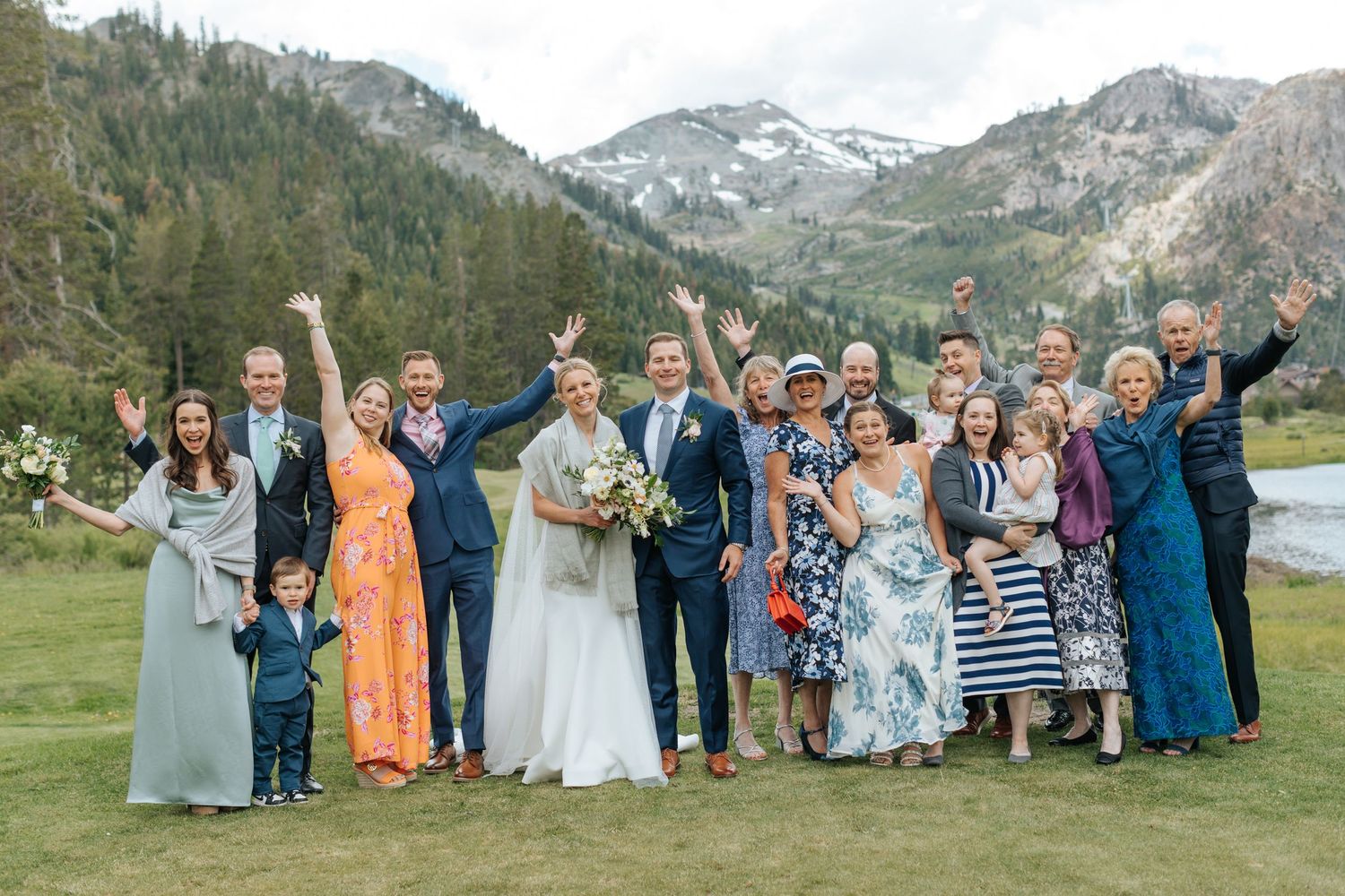 Large wedding group photo with mountains and evergreen trees in background.