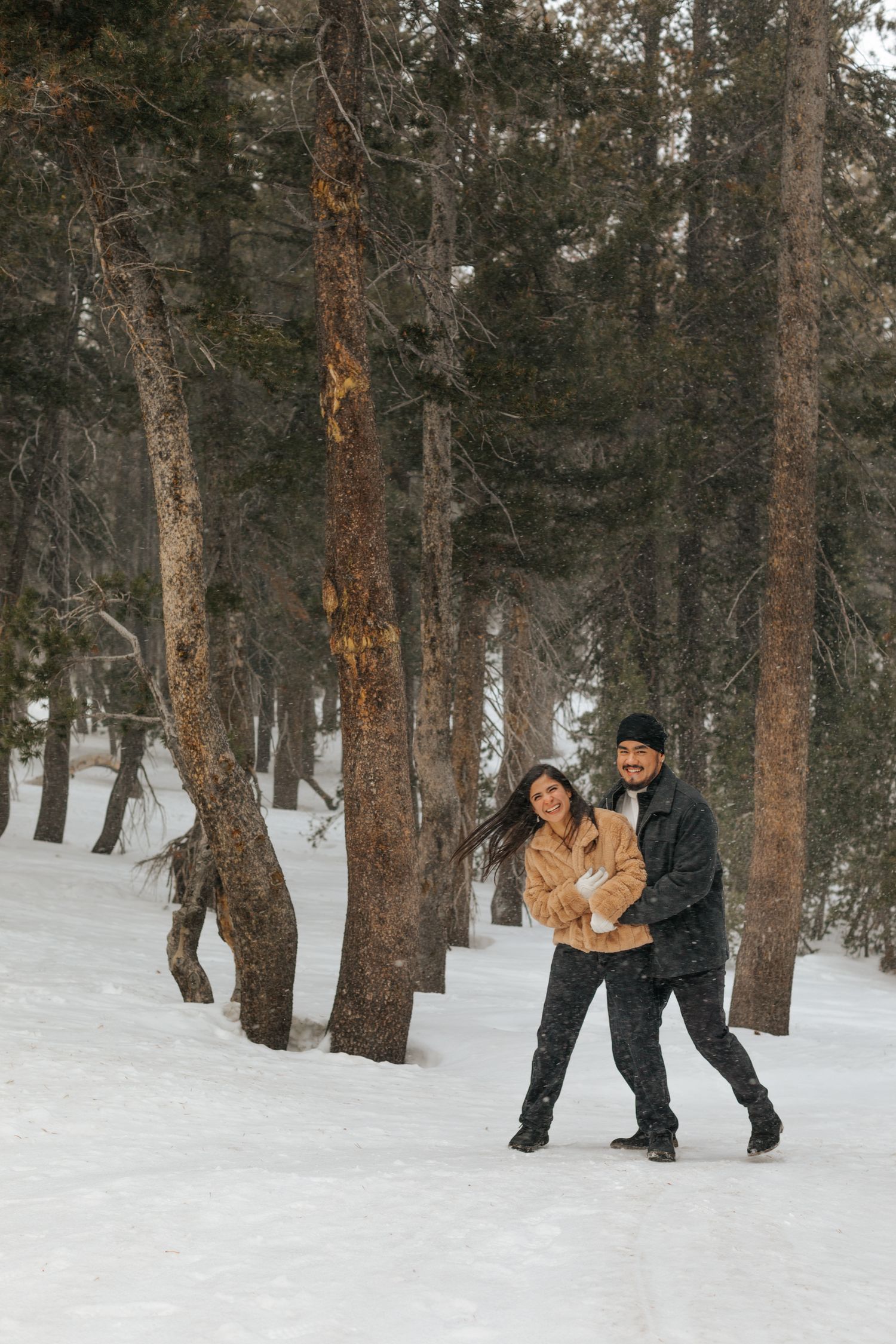 Couple walking through snowy forest holding hands during winter photoshoot.
