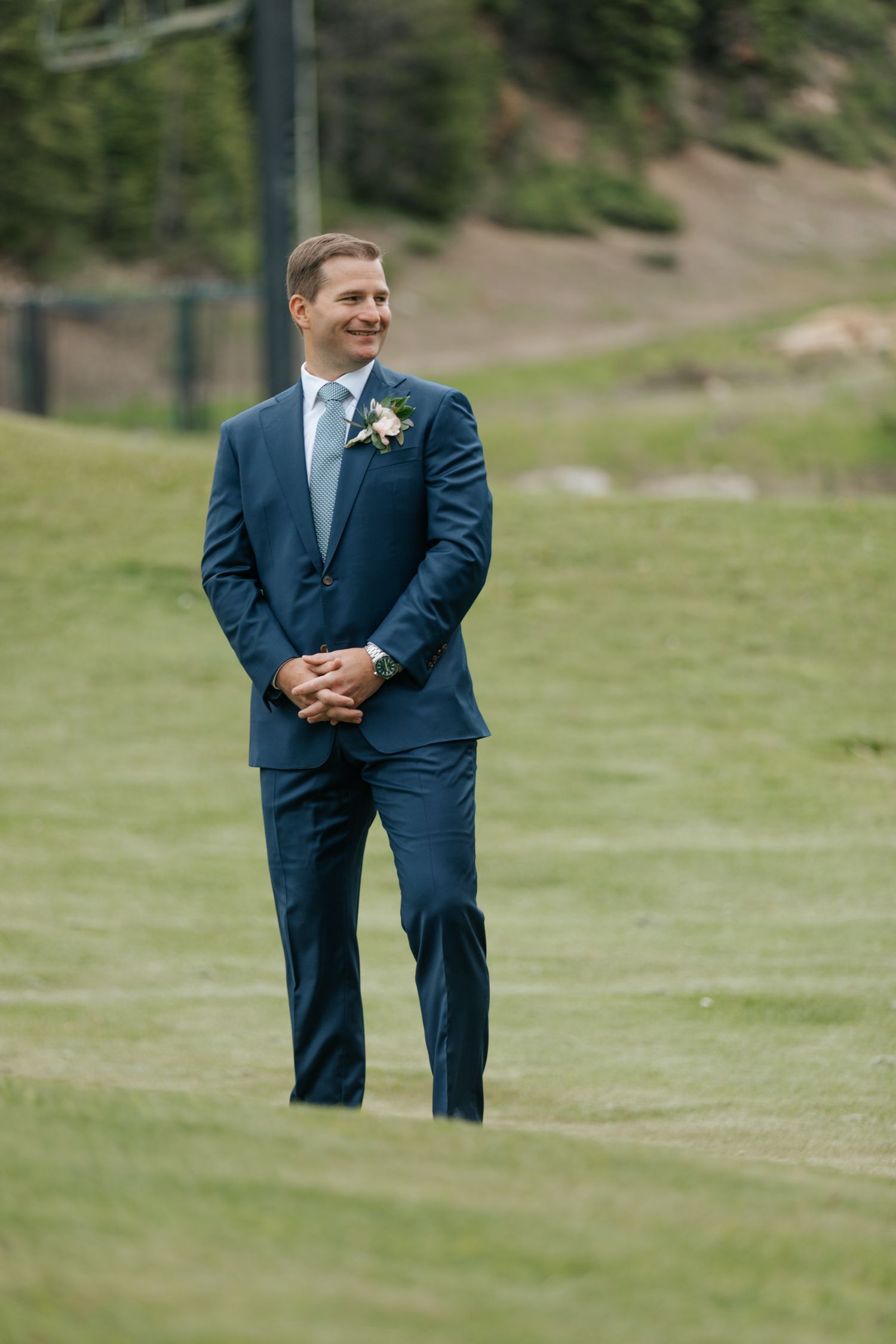 Groomsmen in navy suits standing on grass with mountain scenery in background.