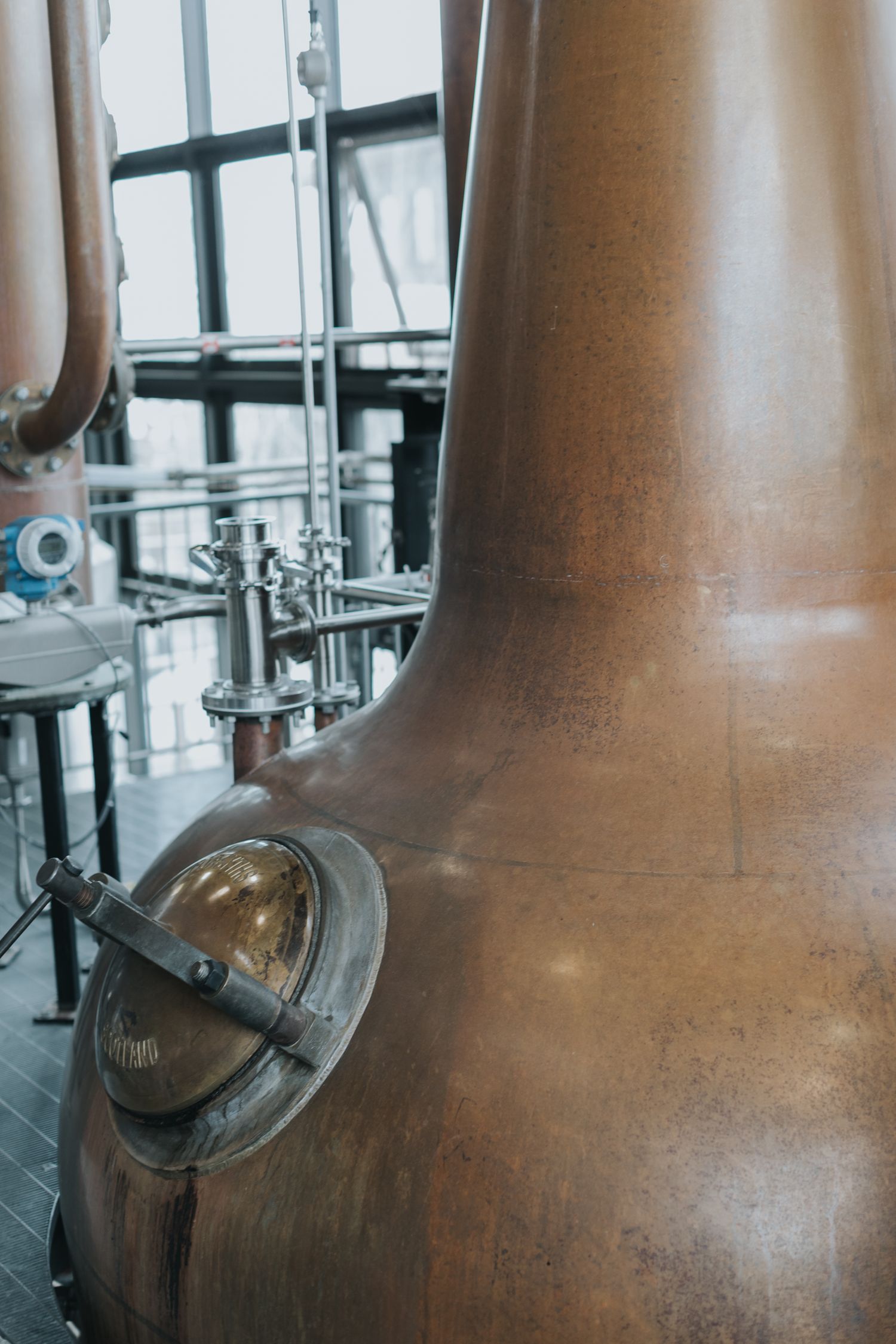Close-up view of copper pot stills with metal piping and connections in a distillery.