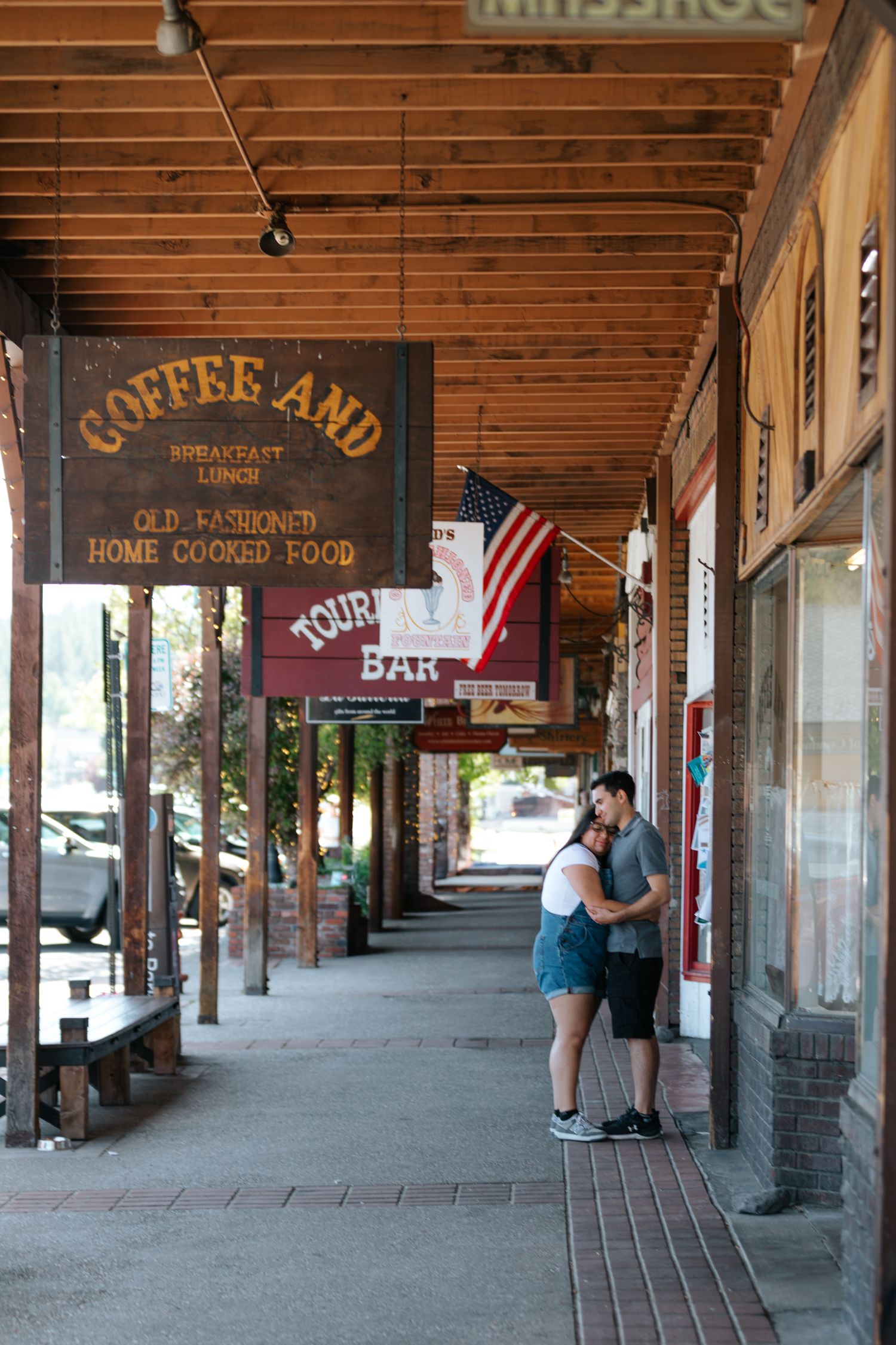 Historic wooden storefront with rustic signs and American flag under covered walkway.