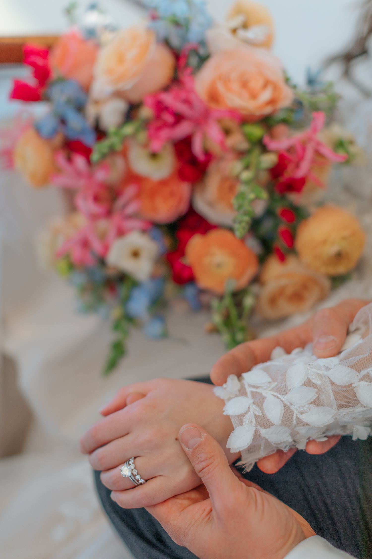 Close-up of engagement ring with colorful peach and pink floral bouquet in background.