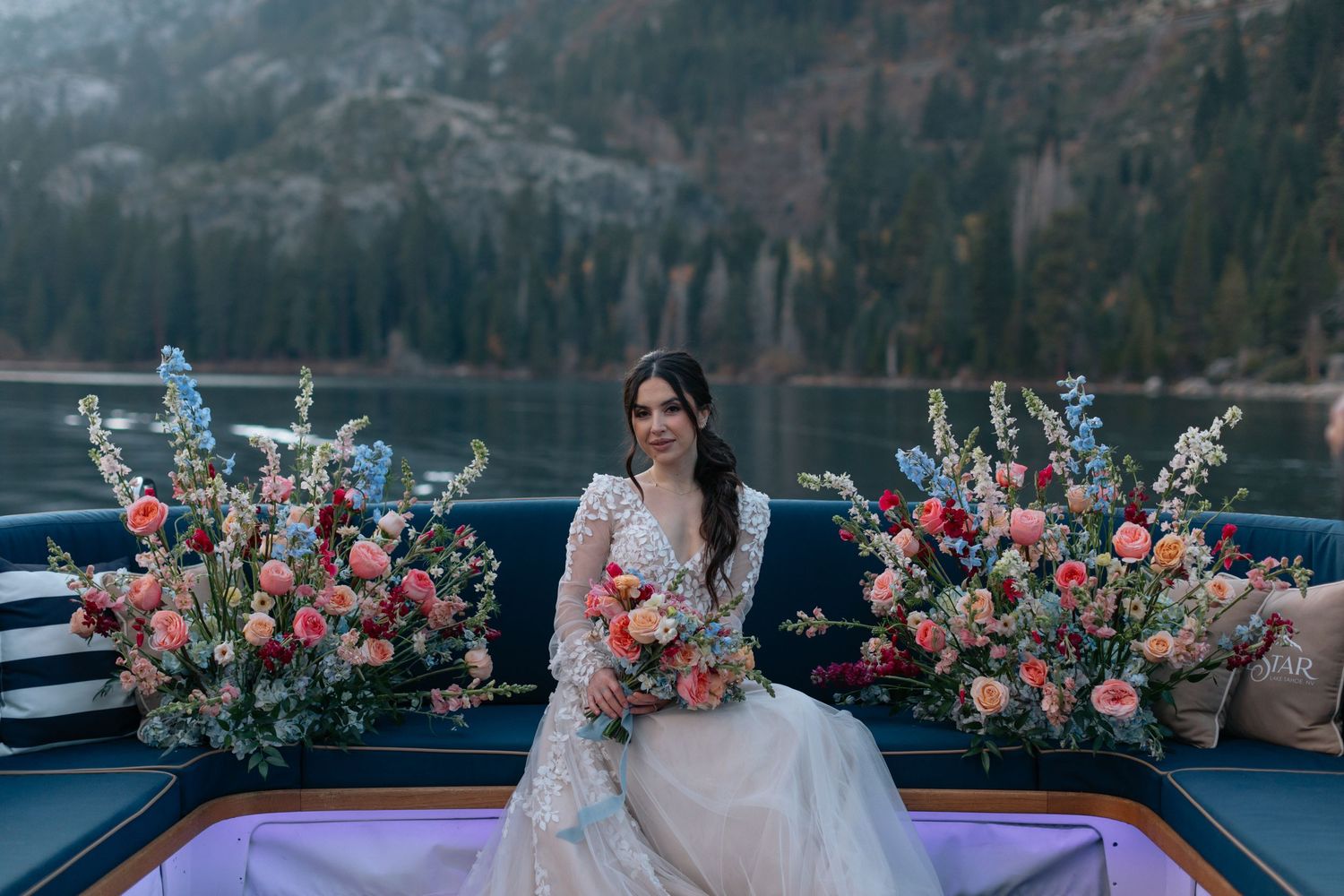 A floral arrangement with pink and coral blooms decorates a boat deck against a mountain backdrop.