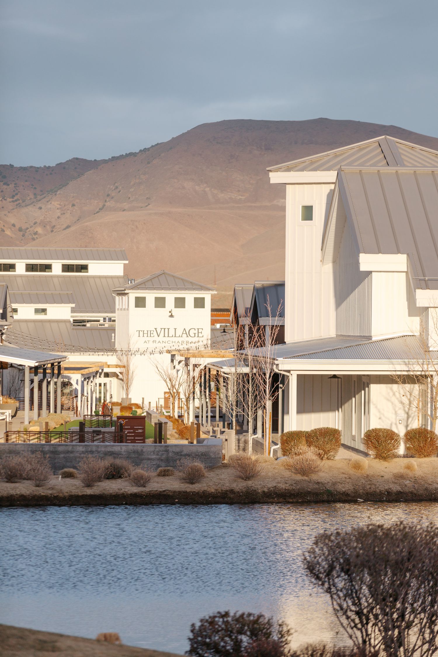 Modern waterfront shopping complex with white buildings against desert mountains.
