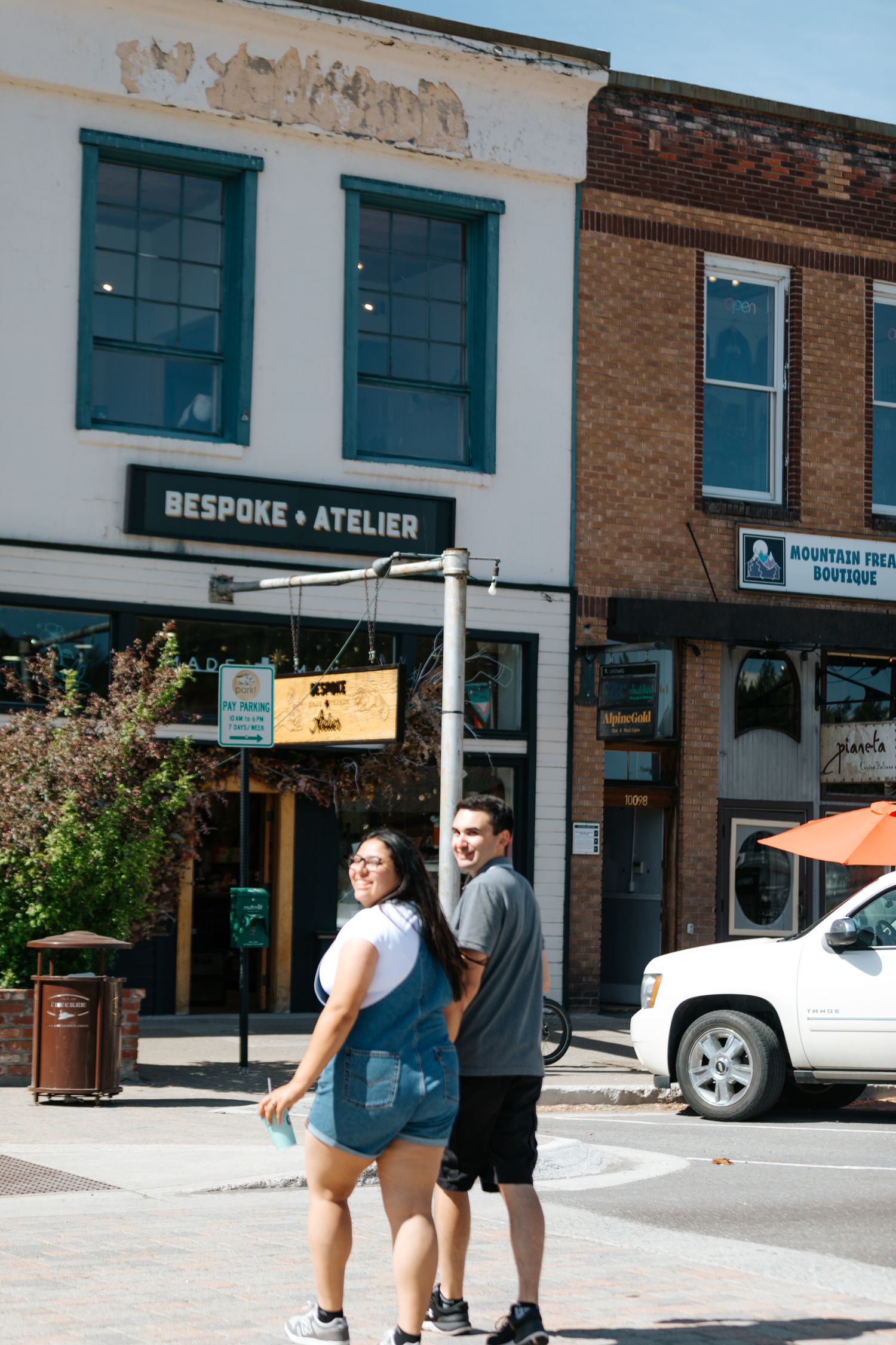Street view of storefronts with a bespoke atelier sign and people walking on sidewalk.