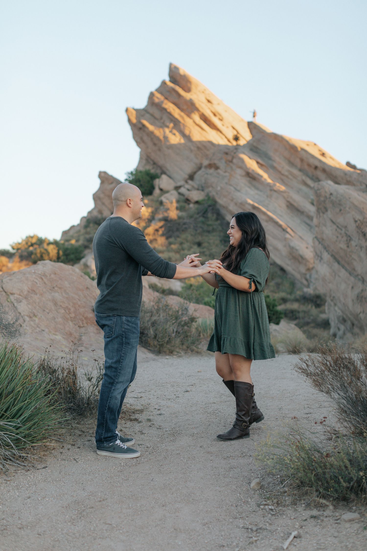 A playful couple dances together on a desert trail with rock formations in the background.